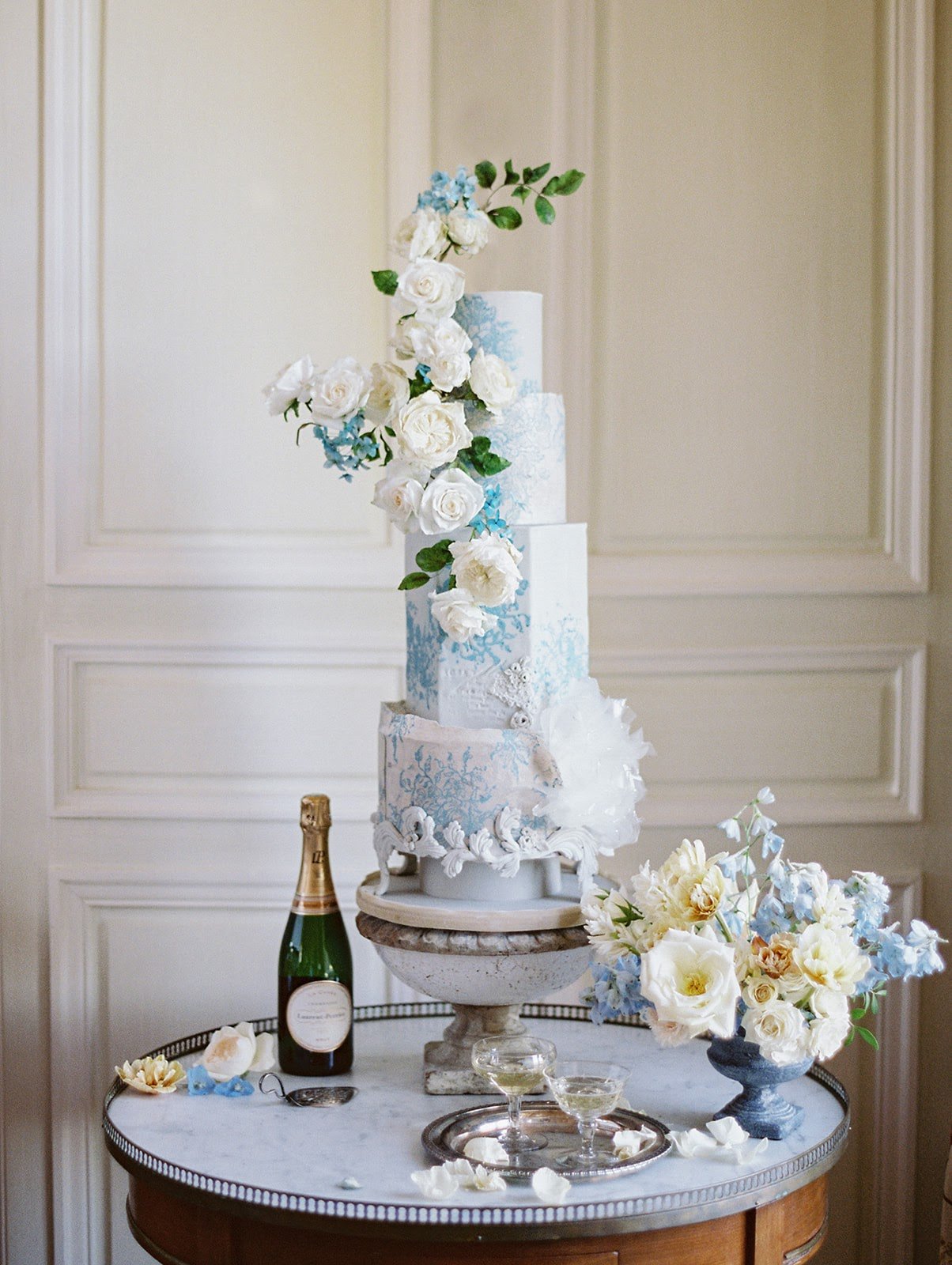 A blue and white  wedding cake, decorated with roses, ready to serve on a table in a Chateau venue.