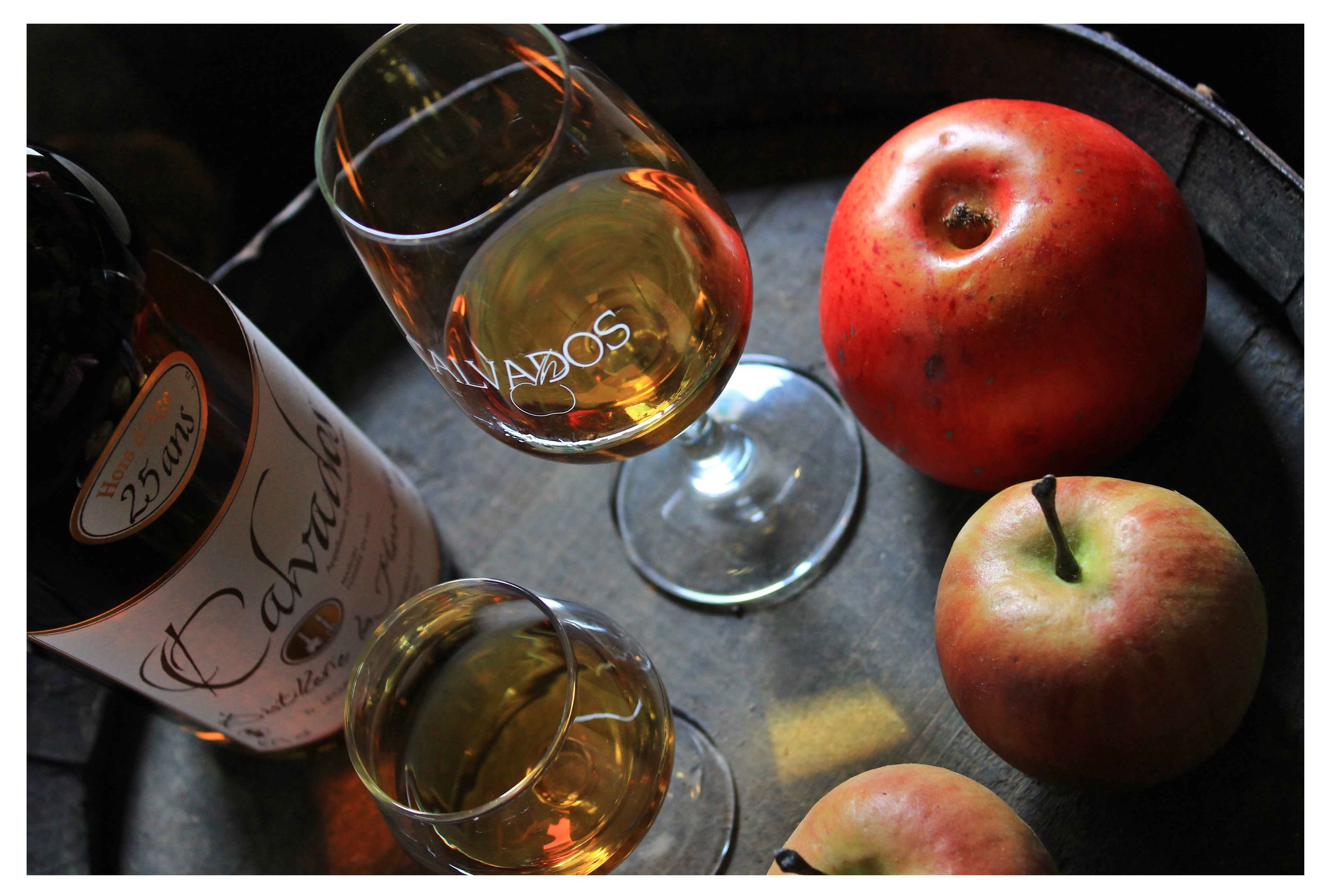 A glass of Calvados on a tray next to apples and the open bottle.