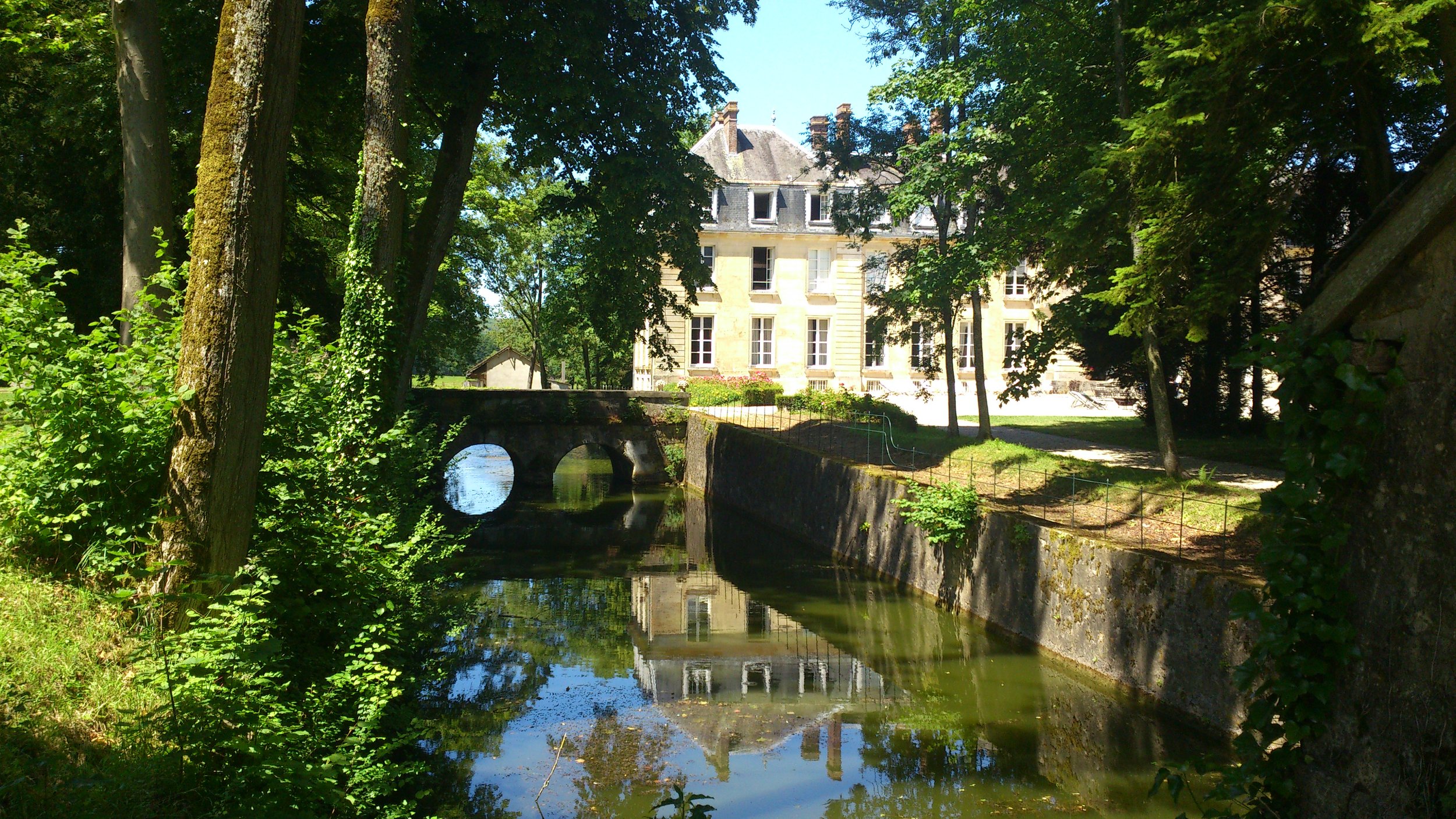 The moat at the rear of Chateau de Courtomer with trees and greenery