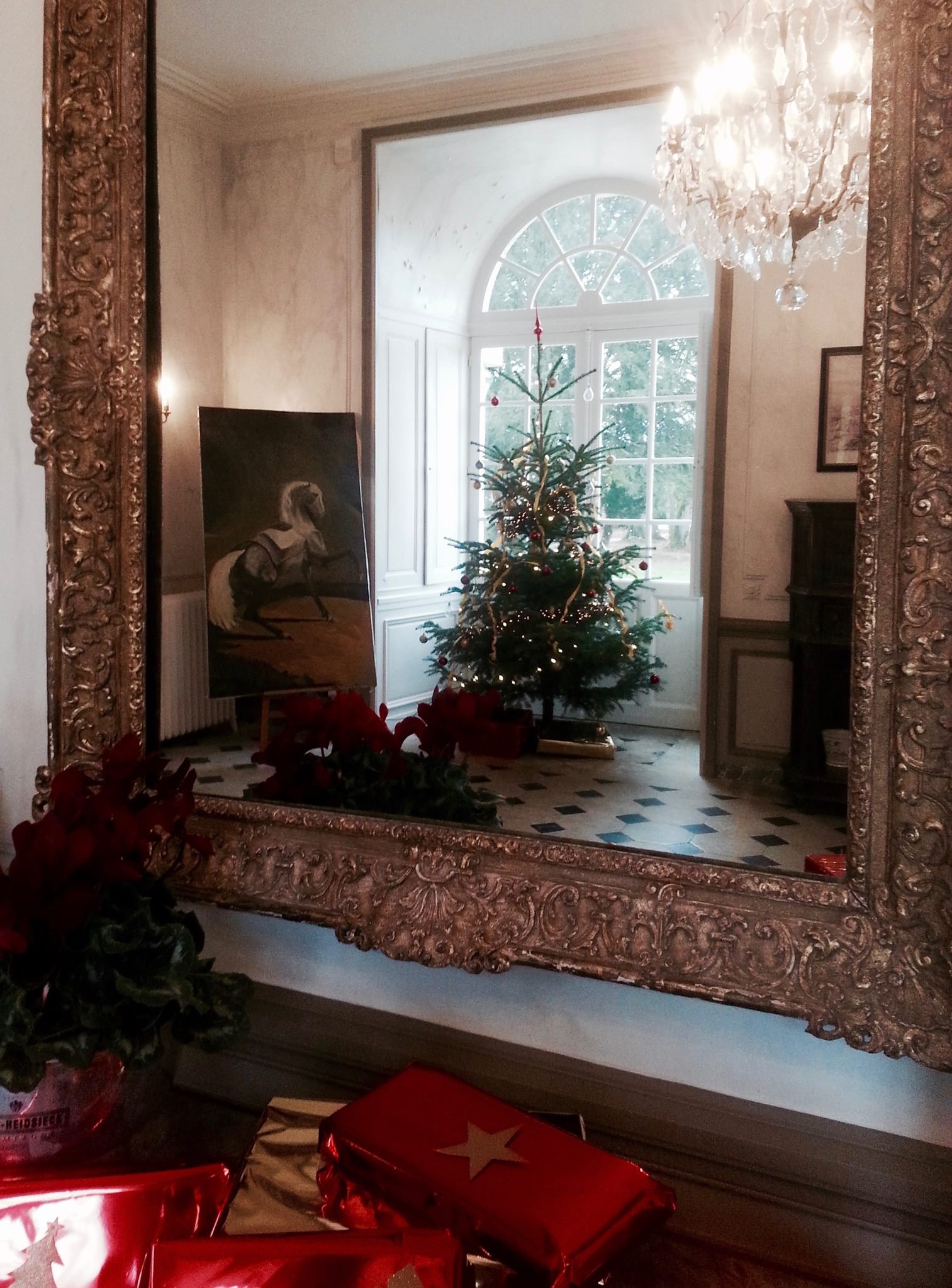 An ornate mirror showing the reflection of a chandelier and a decorated Christmas tree at the Chateau in the holidays.