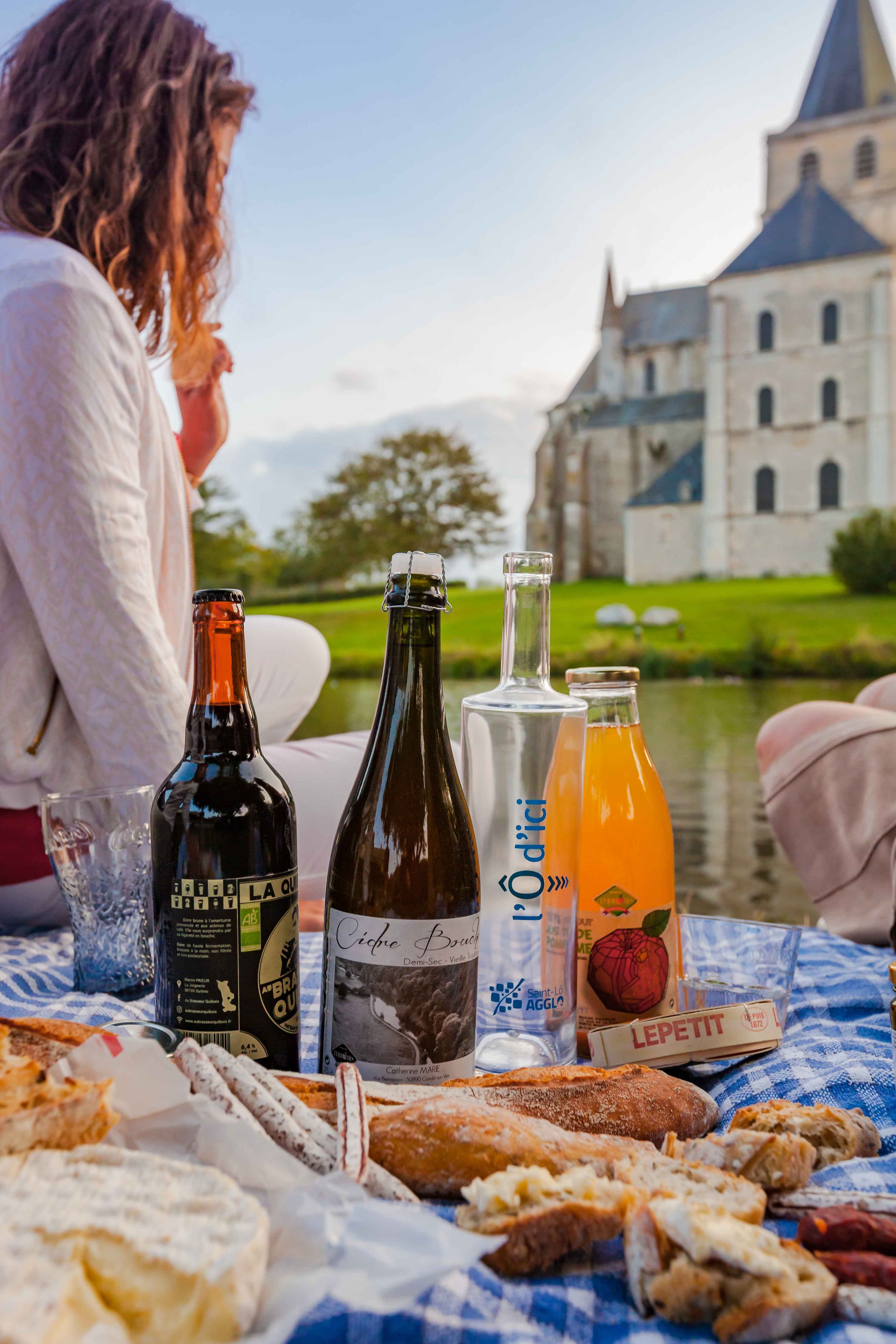 A woman sits on a blanket with food and drinks in front of a French chateau.