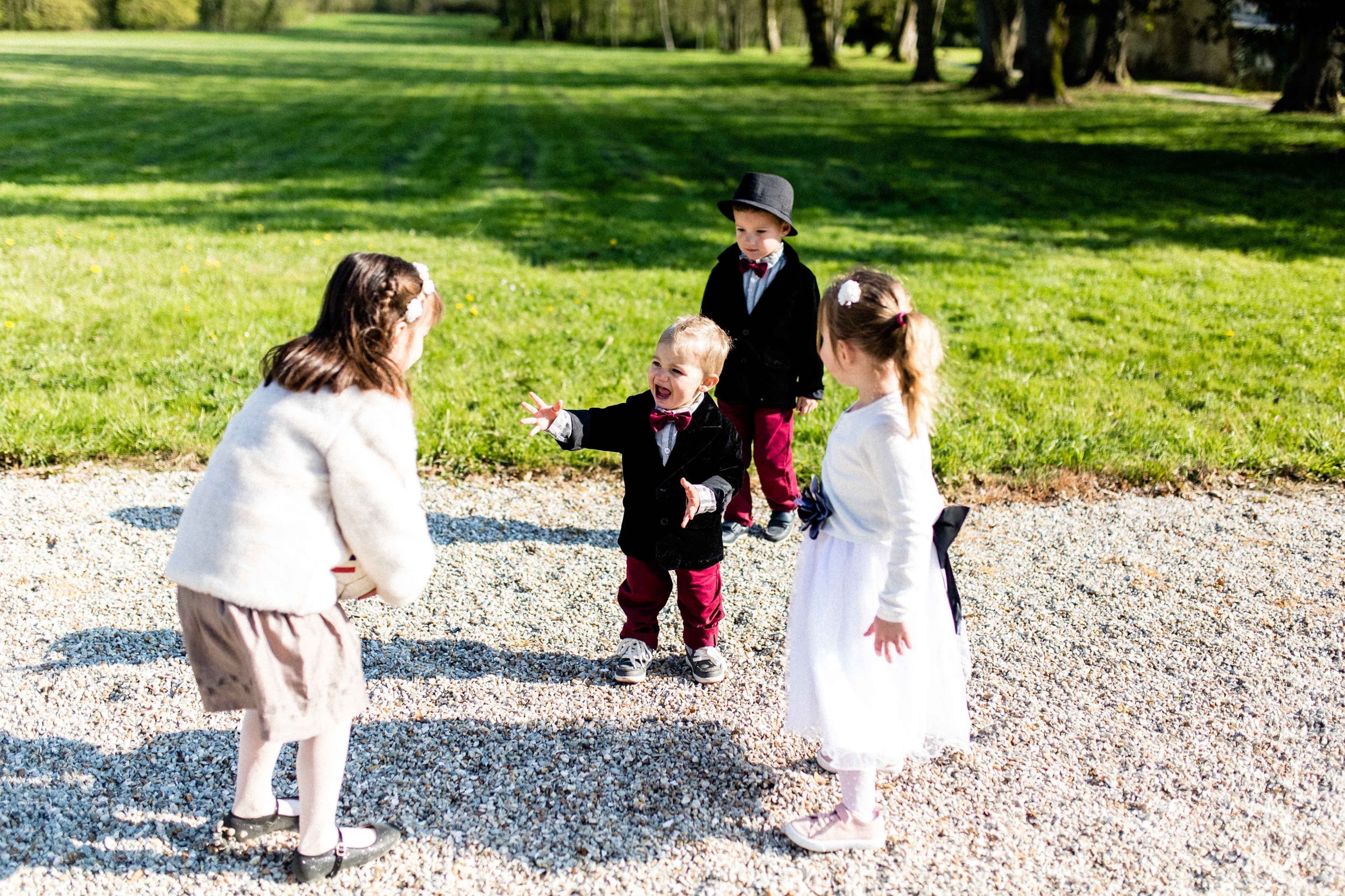 A group of boys and girls in little tuxedos and dresses playing on gravel during a celebration at the chateau.