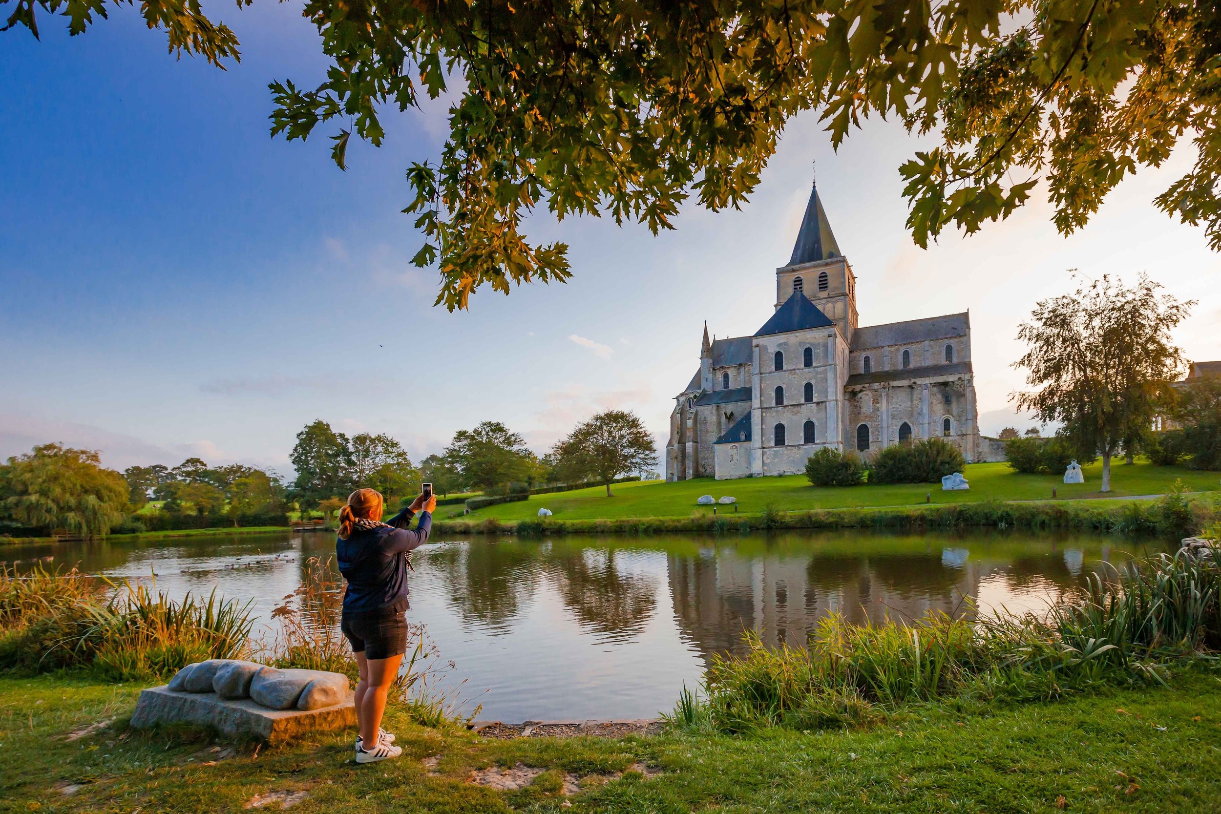 A woman capturing a picture of a building by a lake during her weekend getaway in France.