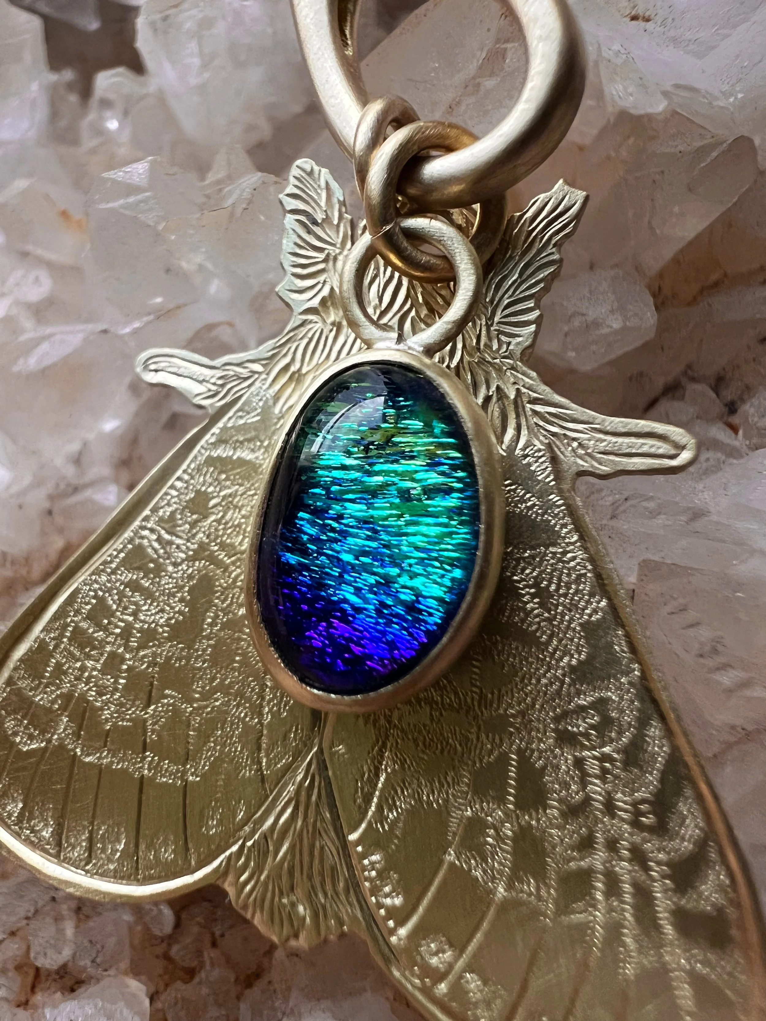 Hand engraved brass moth pendant along side a blue glass pendant