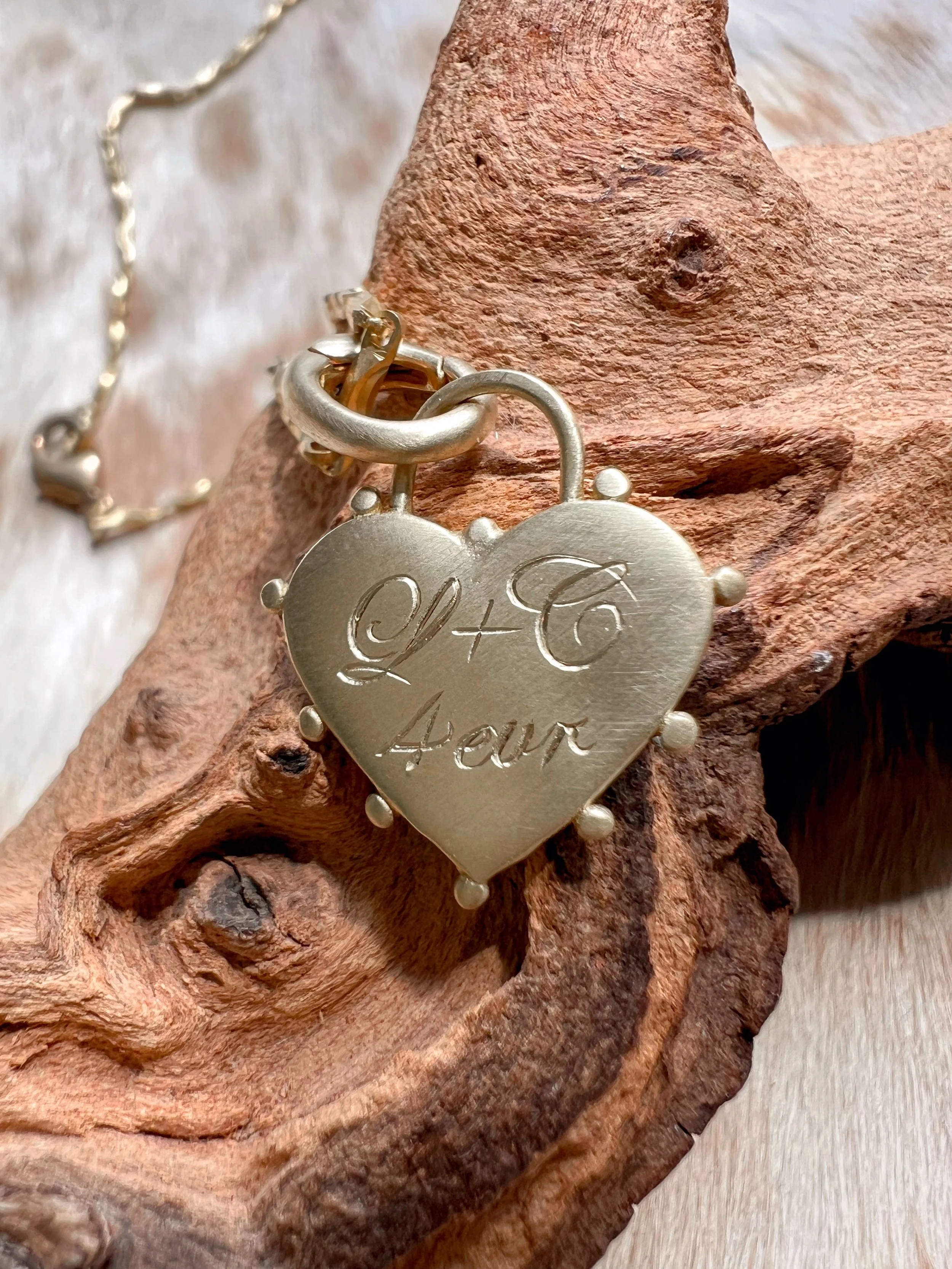 Personalized hand engraved script initials on a small brass heart
