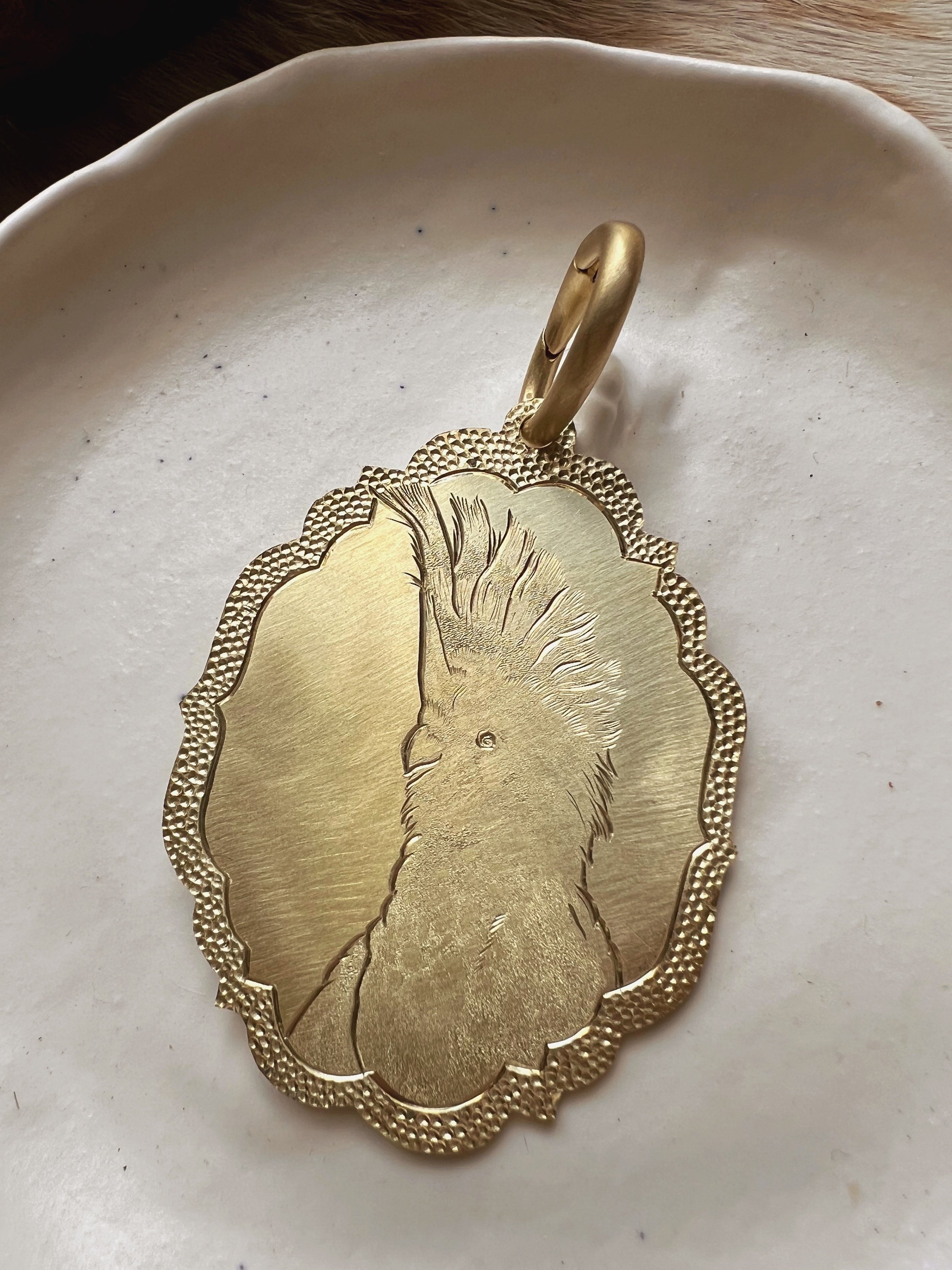 Detailed hand-engraved brass pendant featuring a bird portrait