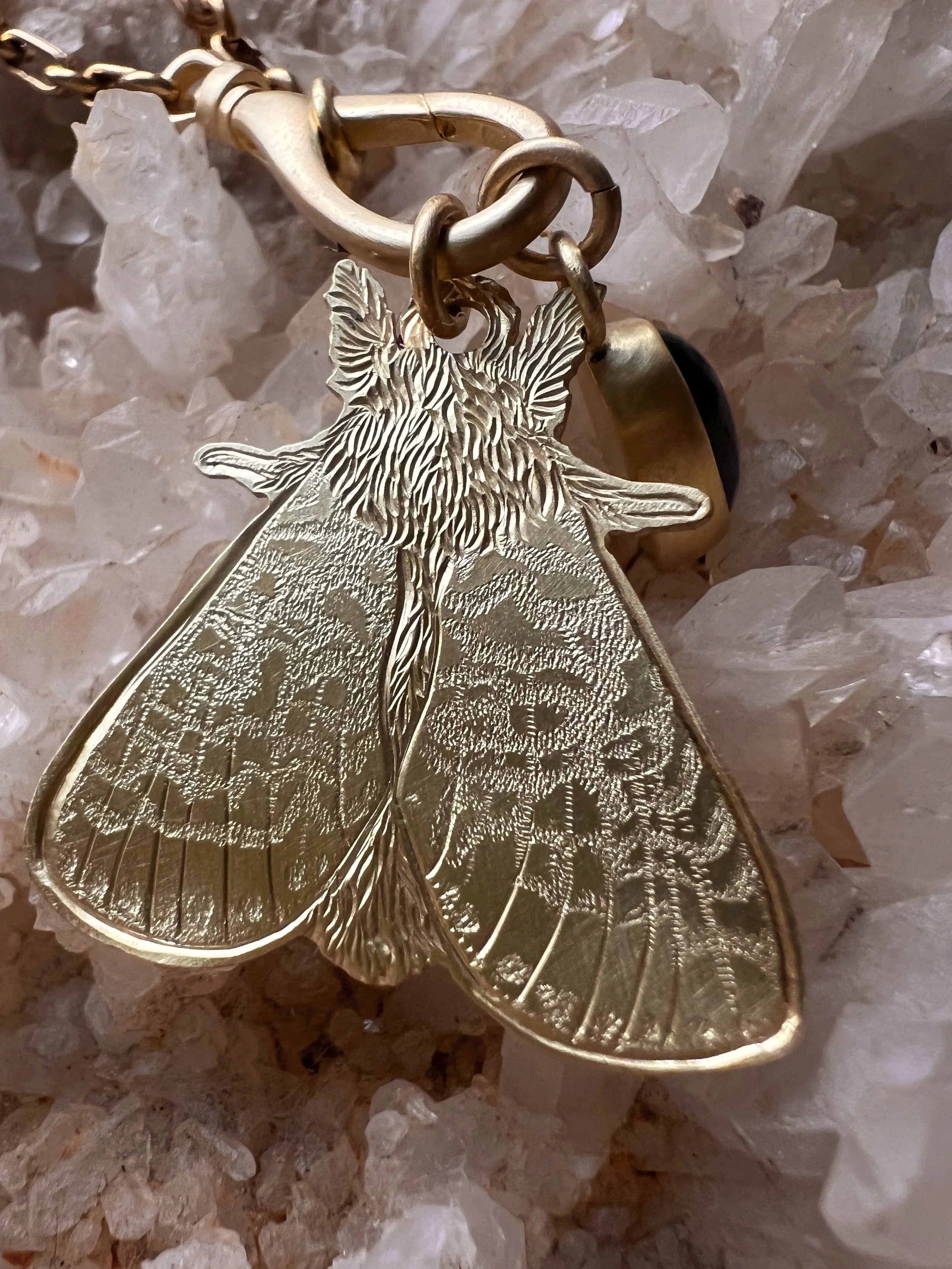 Hand engraved brass moth pendant along side a blue glass pendant