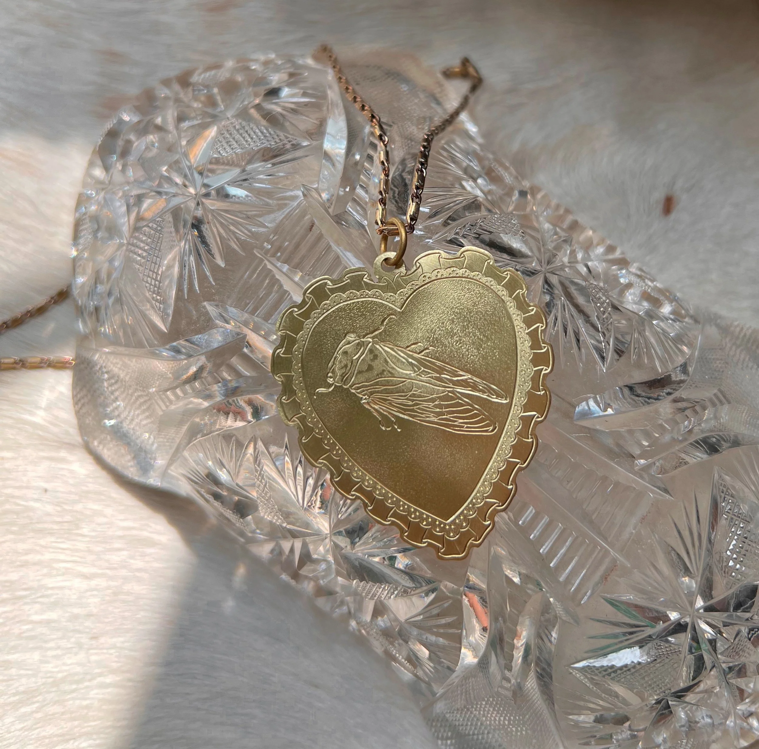 Hand-engraved brass pendant with a cicada in the center of a lacy heart.