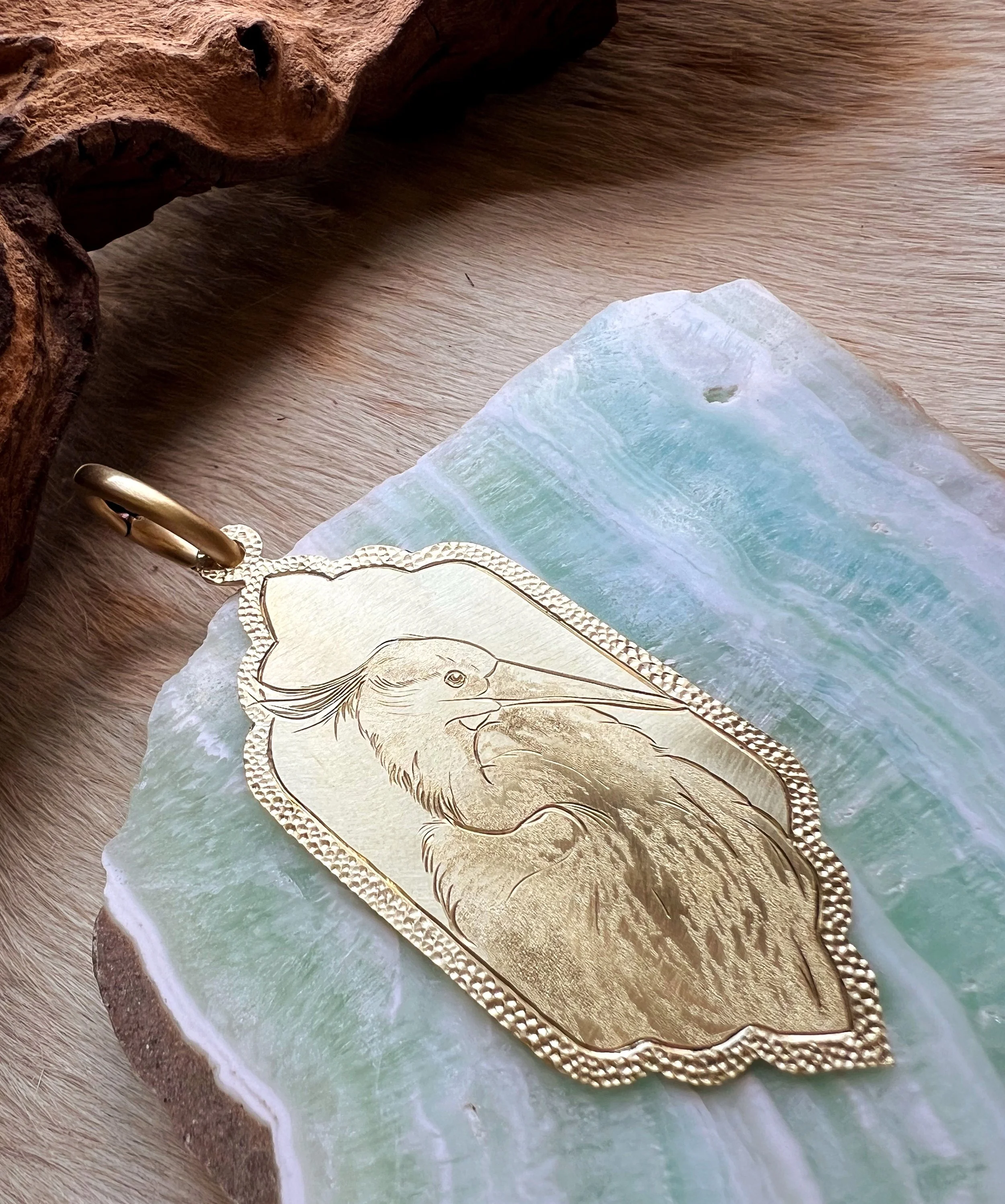 Detailed hand-engraved brass pendant featuring a bird portrait
