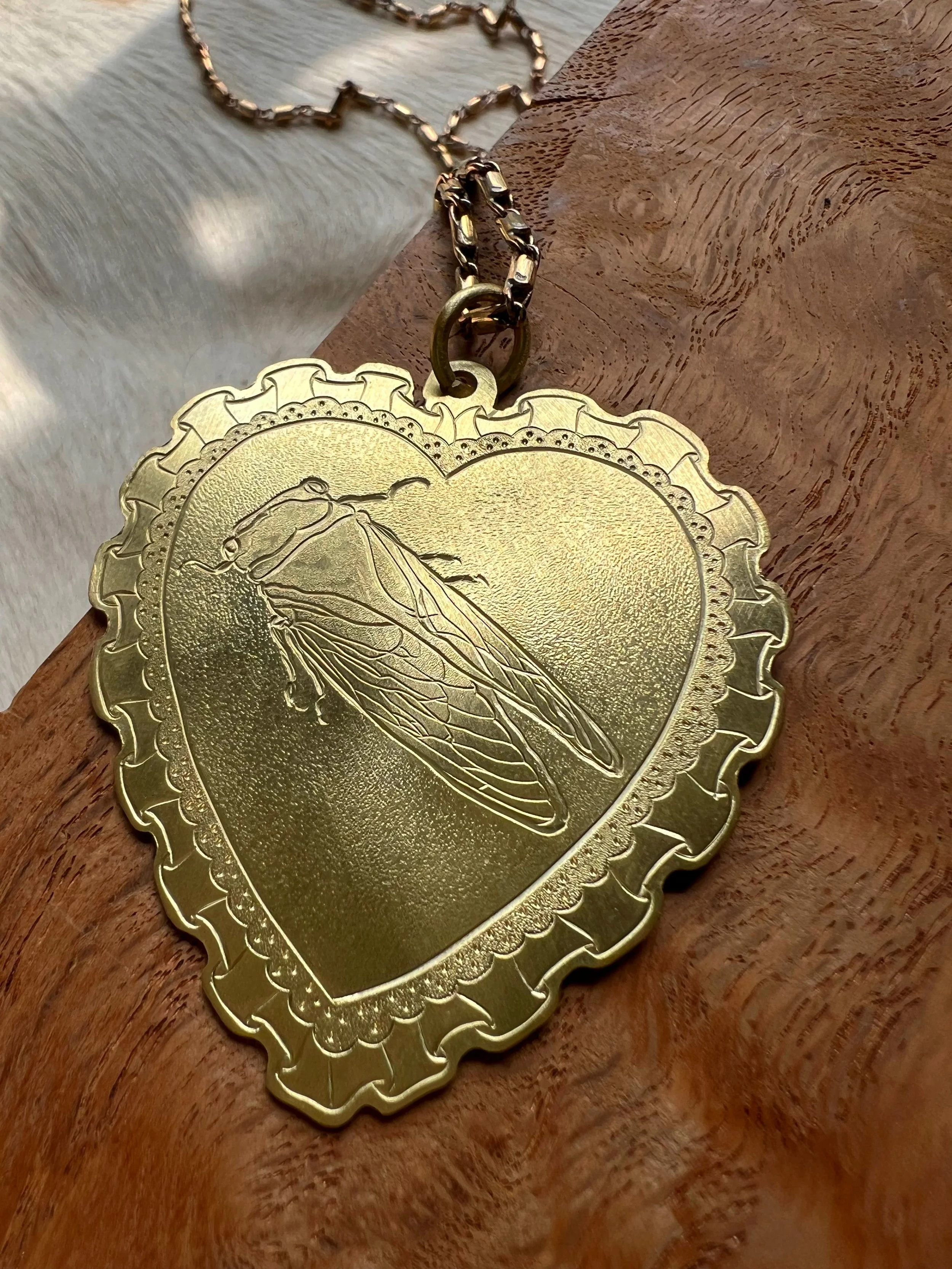 Hand-engraved brass pendant with a cicada in the center of a lacy heart.