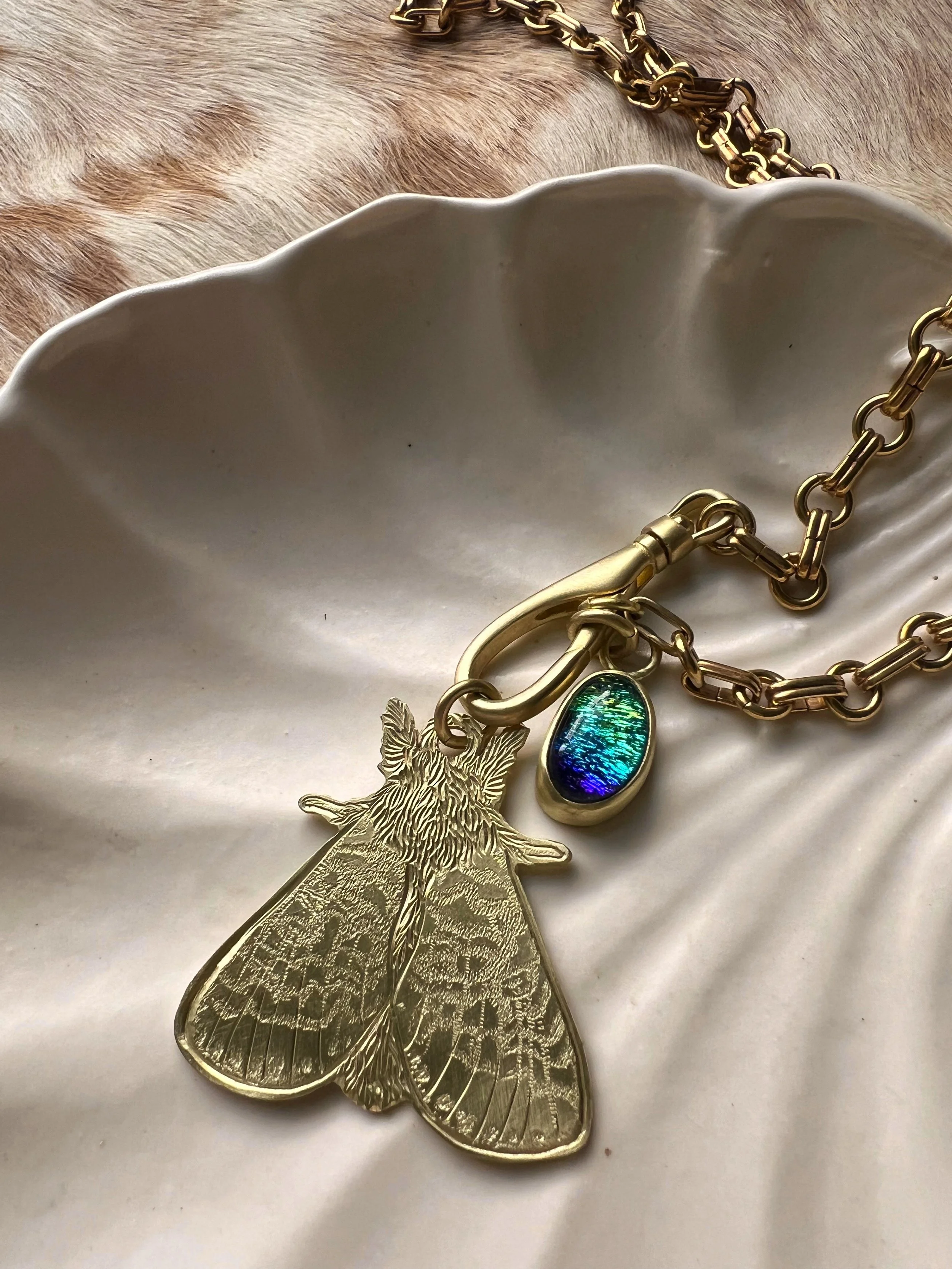 Hand engraved brass moth pendant along side a blue glass pendant