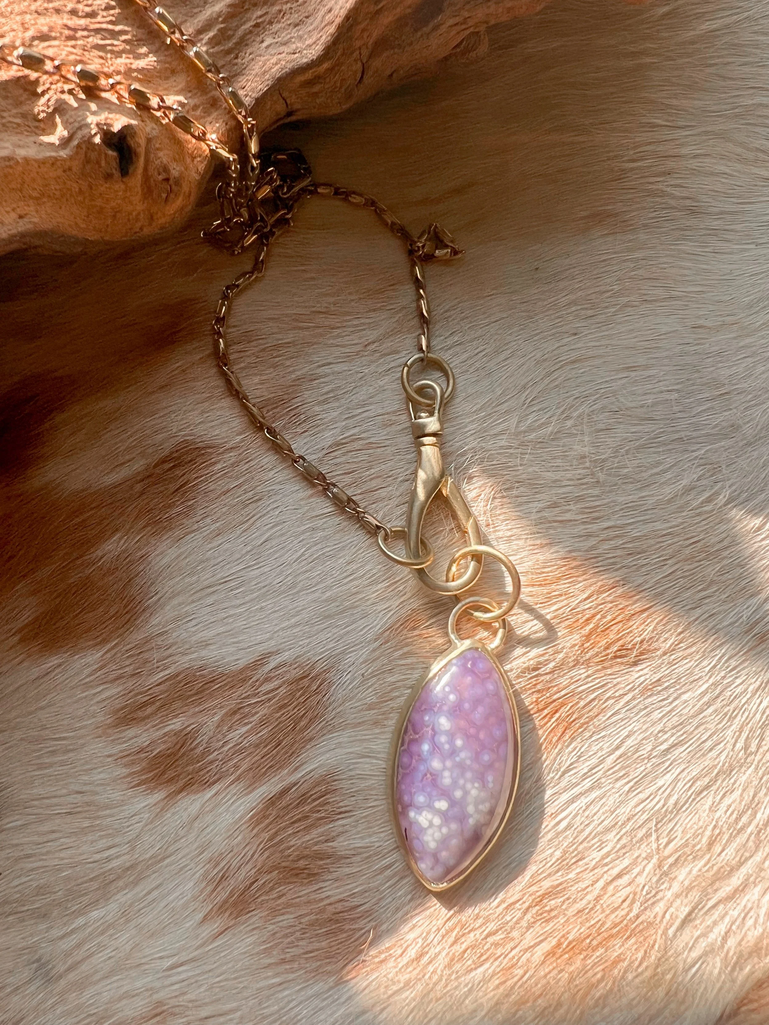 A smooth, natural gemstone cabochon set in a brass pendant on a brass chain.