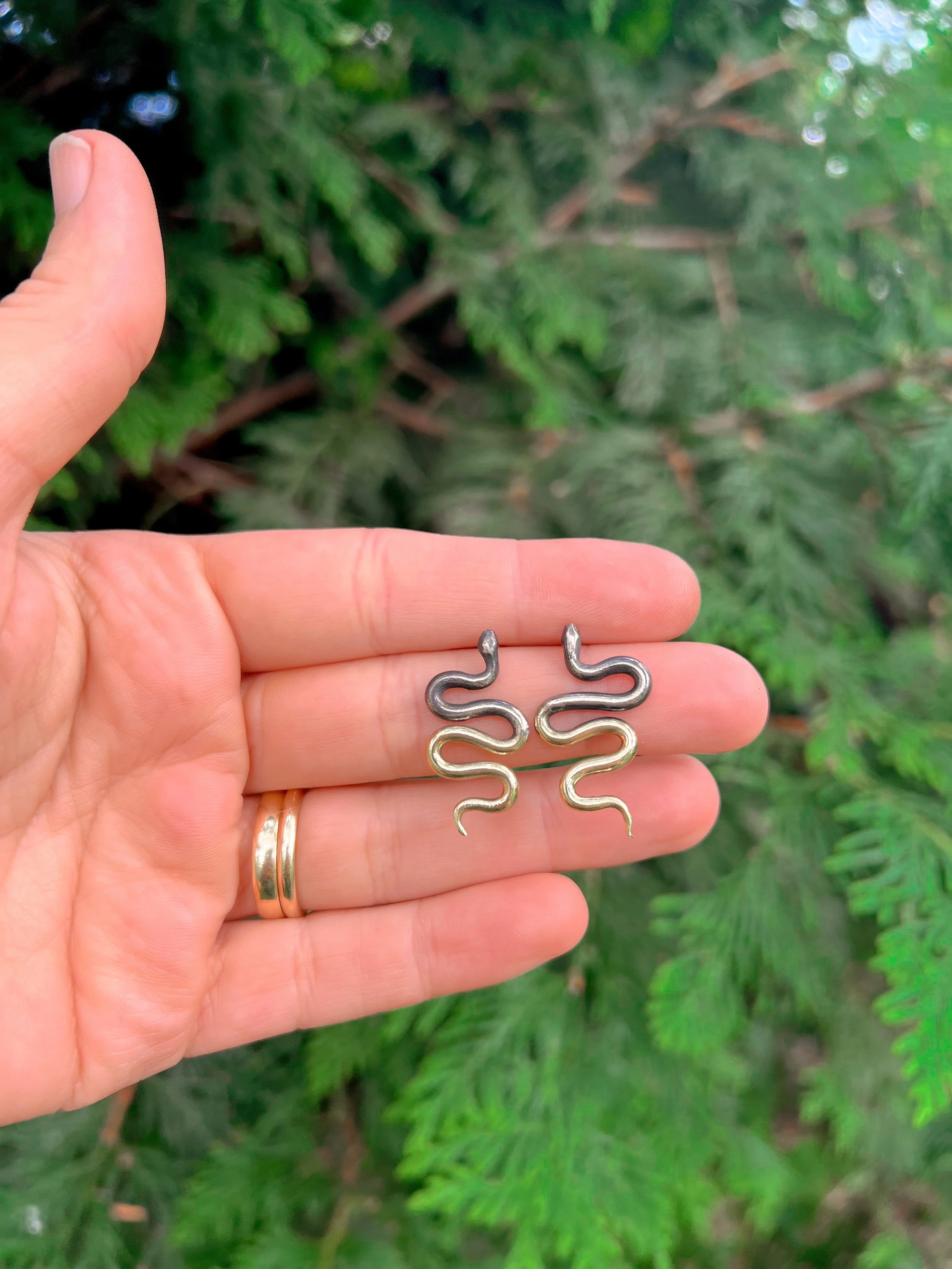 A pair of snake earrings made of oxidized silver fading to brass with sterling silver posts and backs