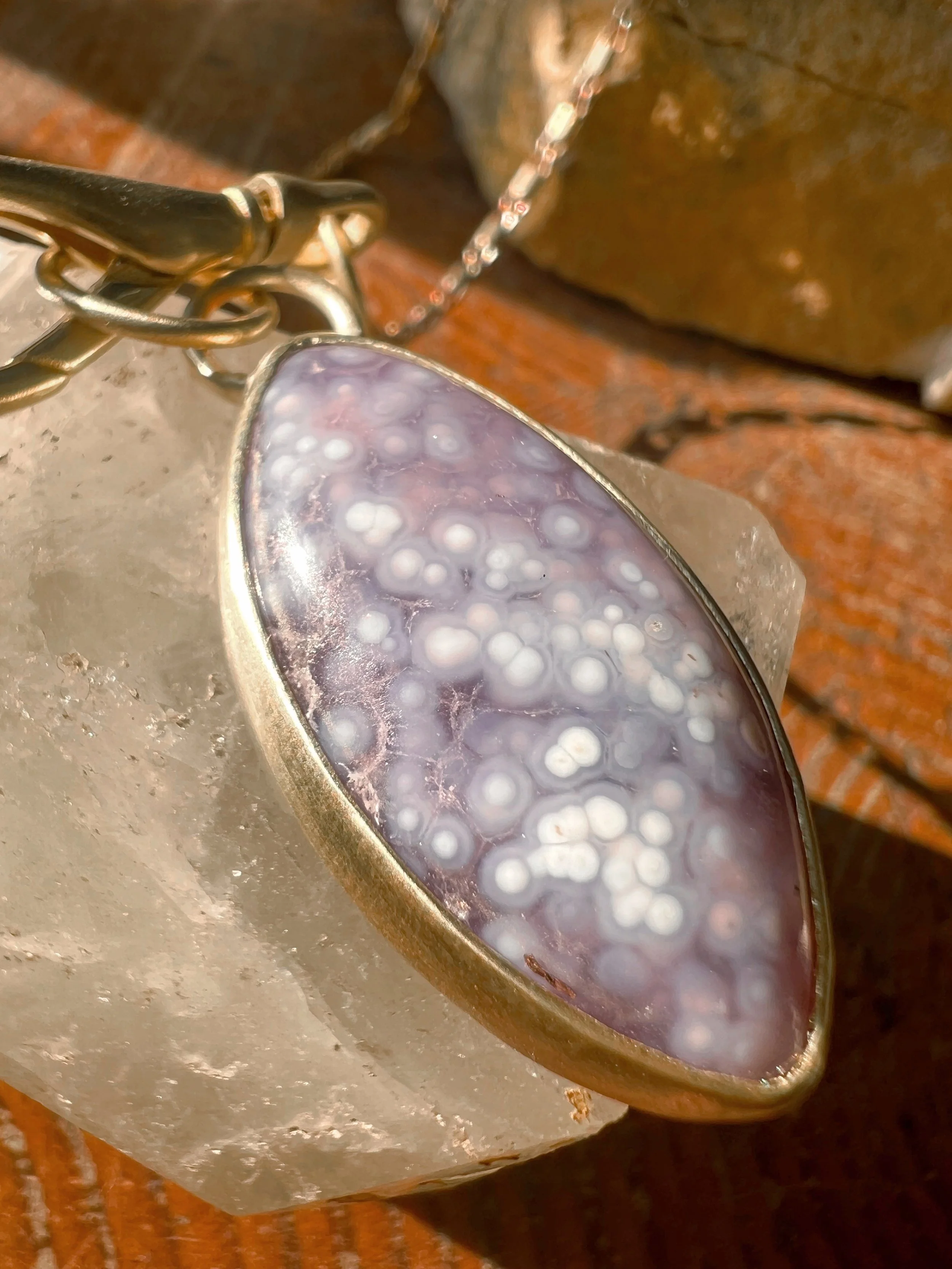 A smooth, natural gemstone cabochon set in a brass pendant on a brass chain.