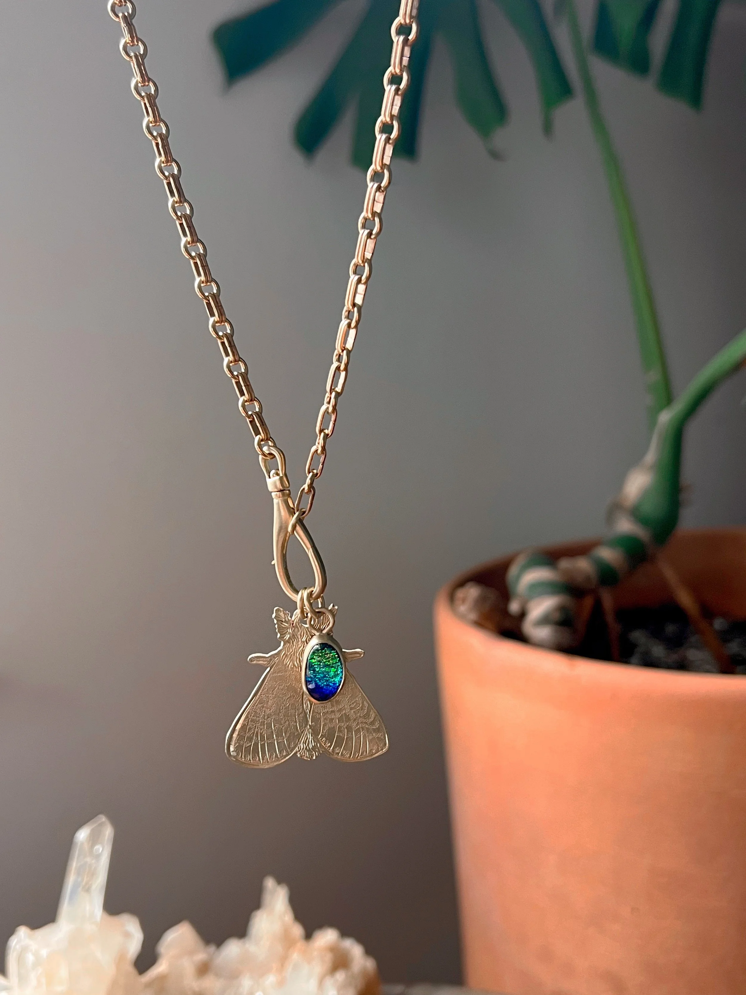 Hand engraved brass moth pendant along side a blue glass pendant