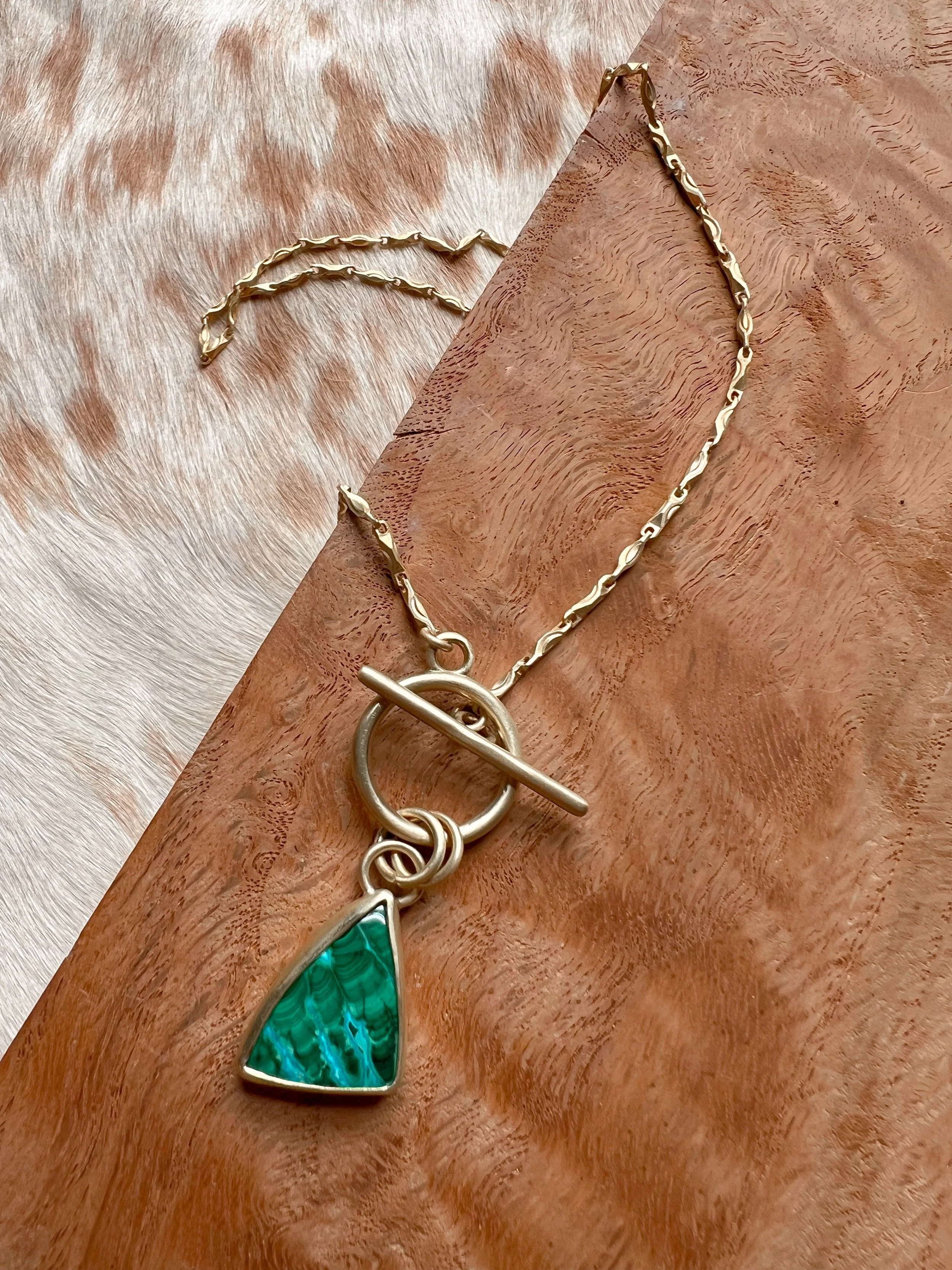 A smooth, natural gemstone cabochon set in a brass pendant on a brass chain.