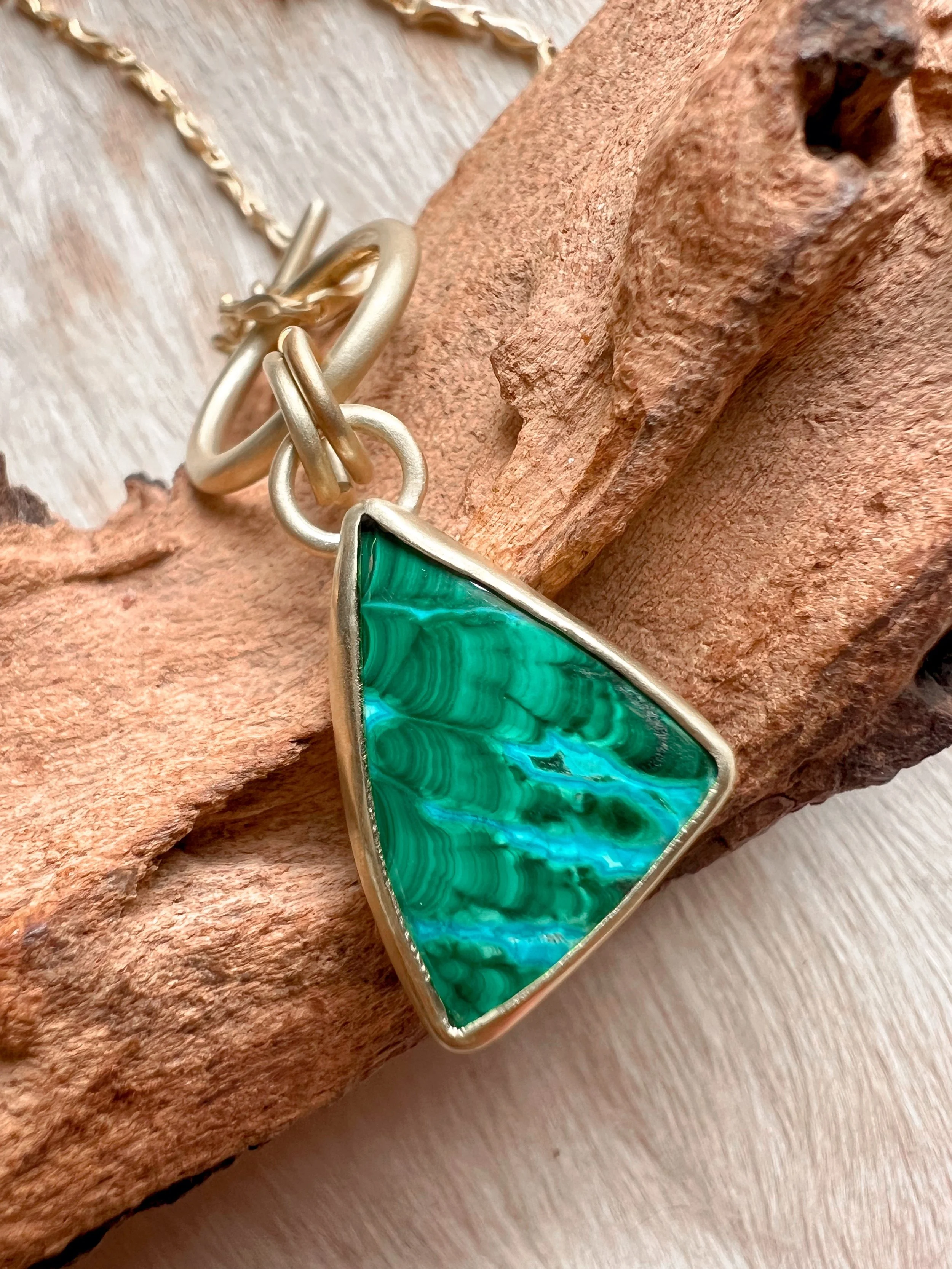 A smooth, natural gemstone cabochon set in a brass pendant on a brass chain.
