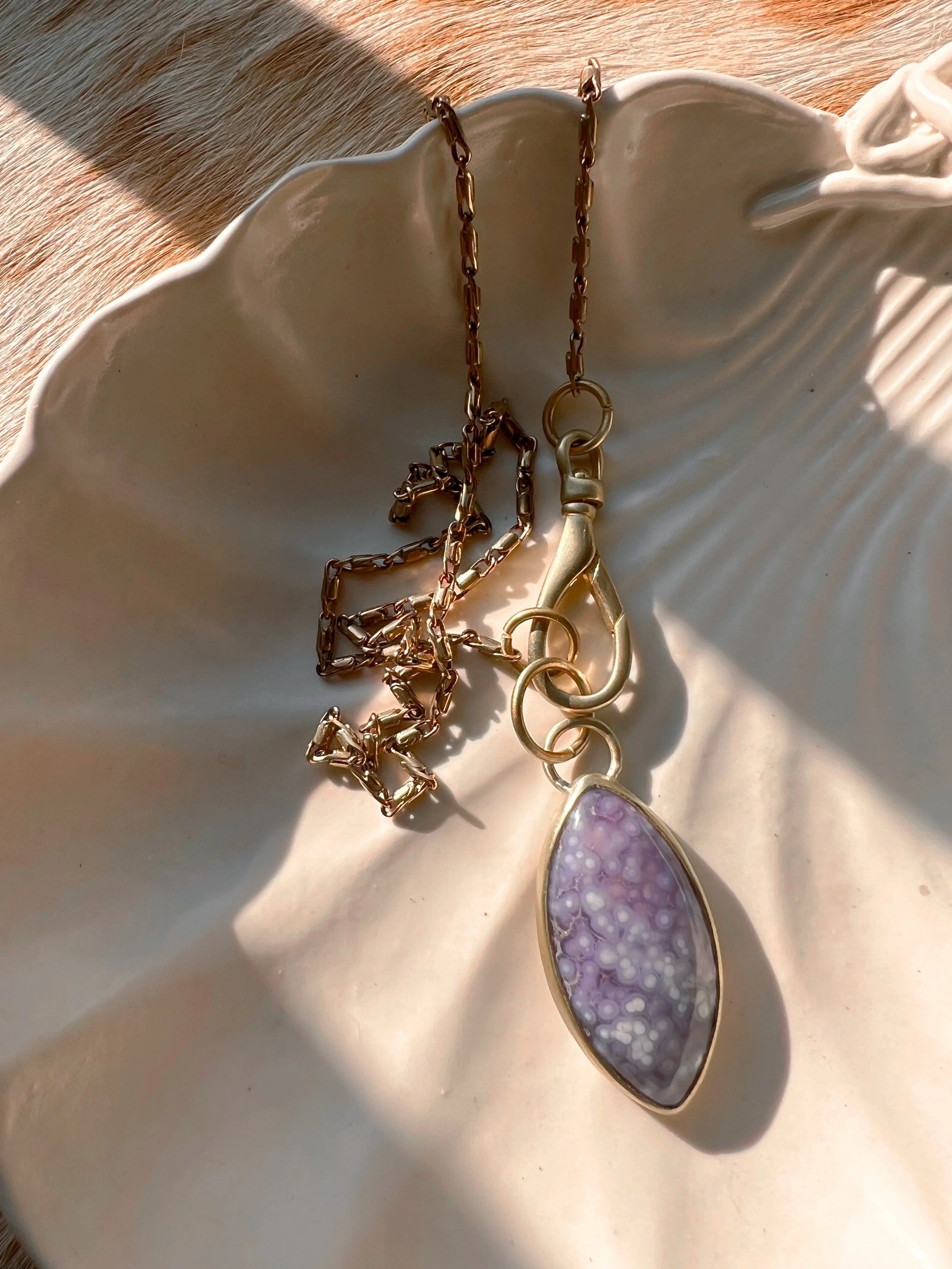 A smooth, natural gemstone cabochon set in a brass pendant on a brass chain.