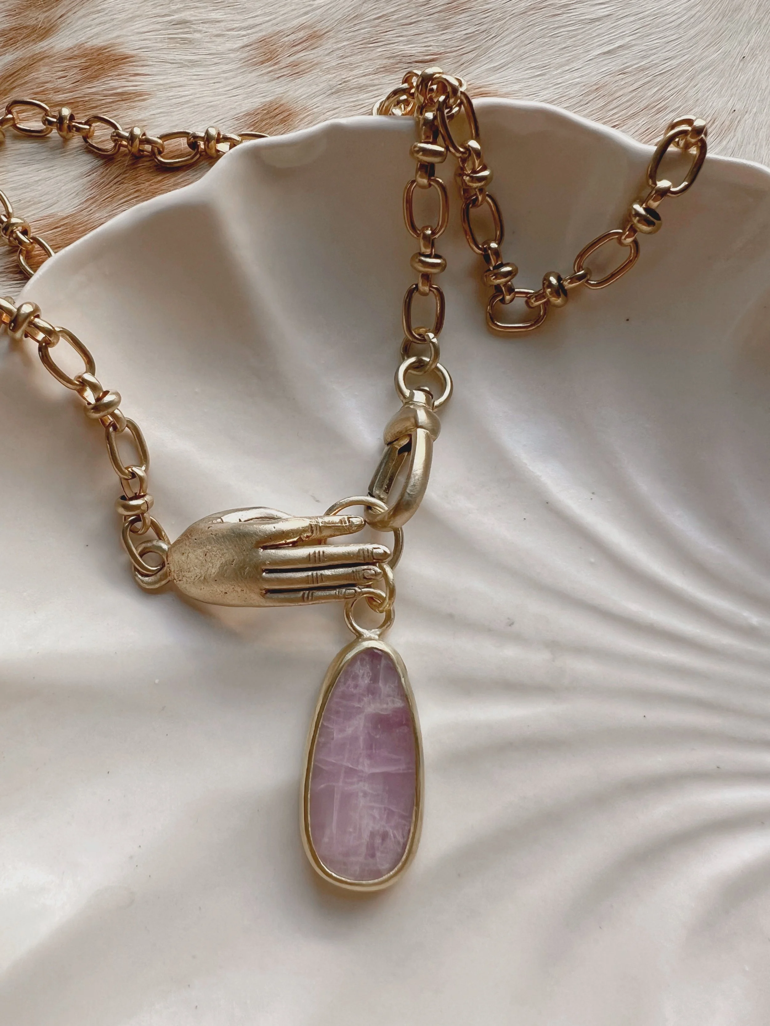 A smooth, natural gemstone cabochon set in a brass pendant on a brass chain.