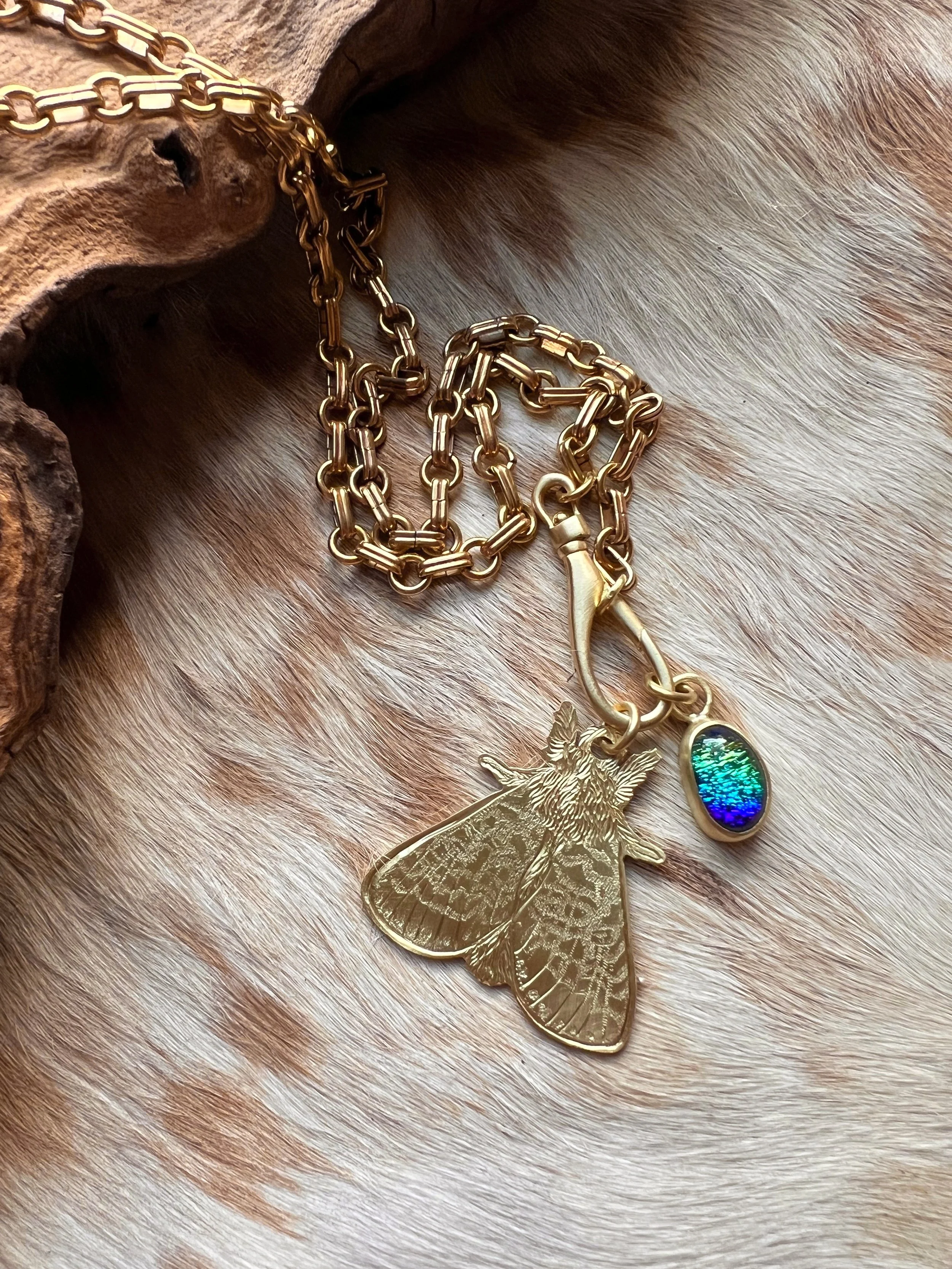 Hand engraved brass moth pendant along side a blue glass pendant