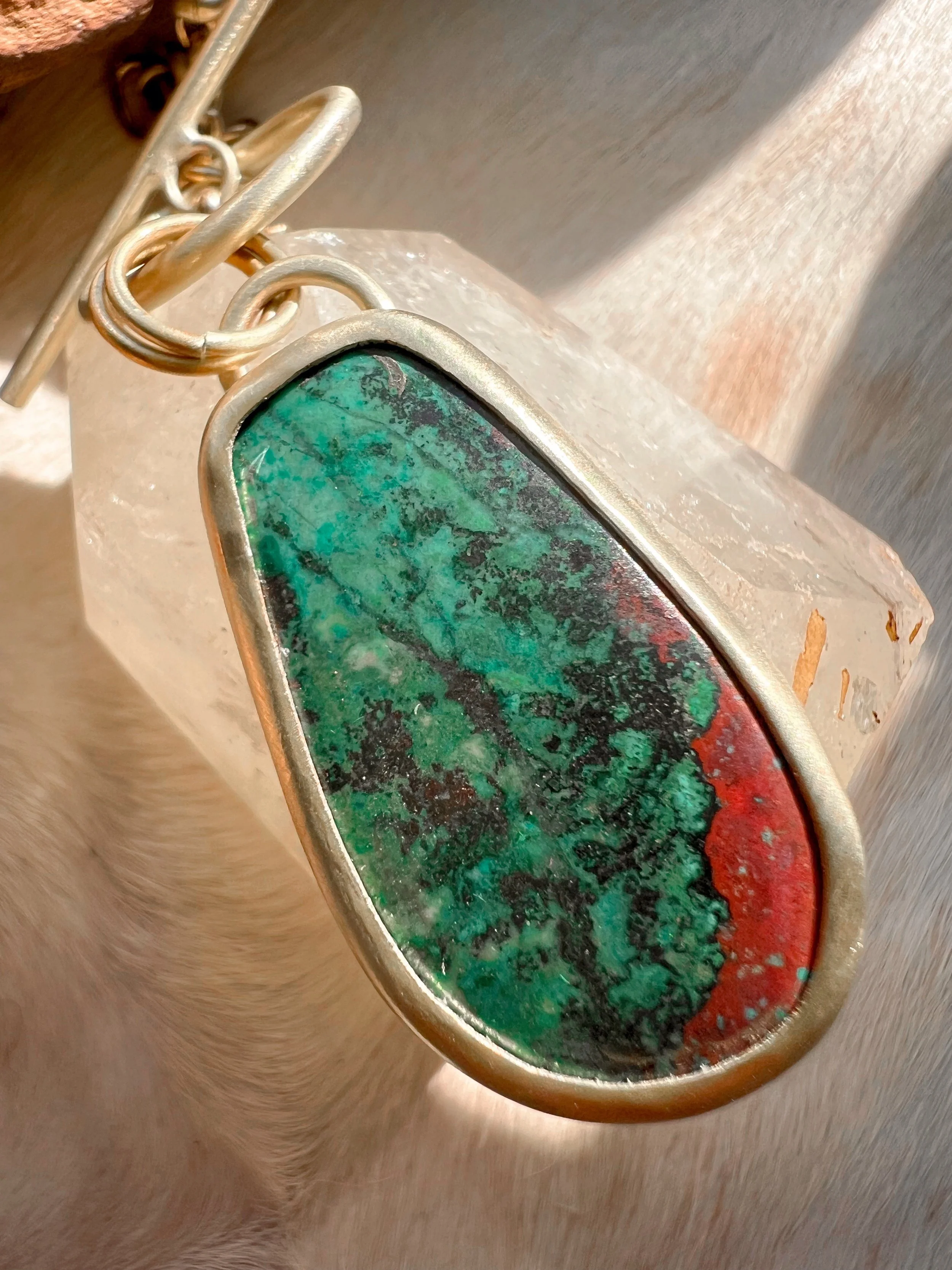 A smooth, natural gemstone cabochon set in a brass pendant on a brass chain.