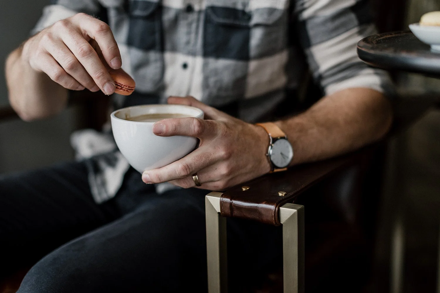 Image of a man in a plaid shirt wearing a leather watch, stirring coffee in a white mug. Photography by Michael Carr. Brand strategy by Clarke Creative for Architectural Justice.