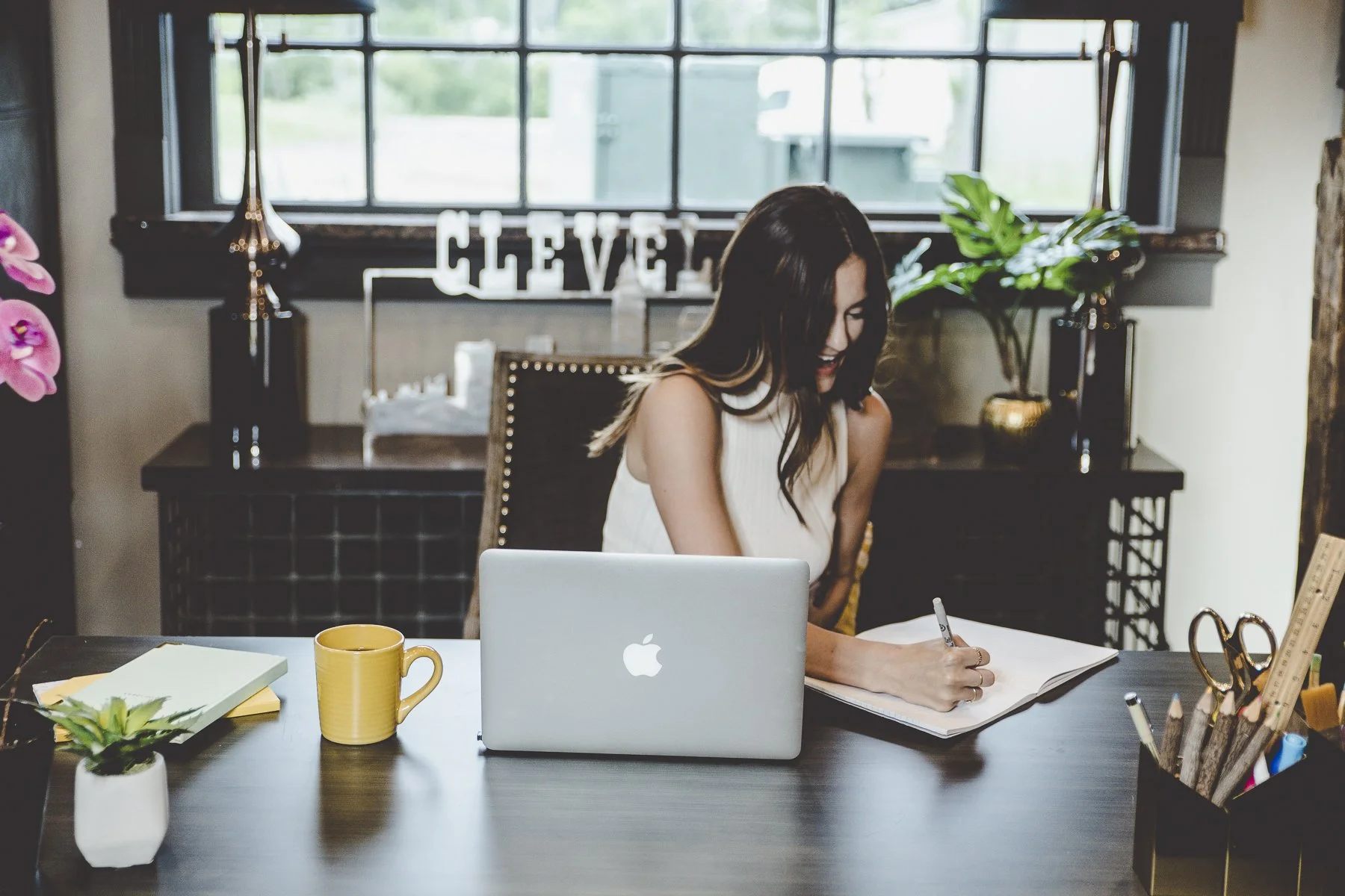 Rachelle Clarke, smiling and writing in a notebook with a laptop in front of her, working at her brand strategy studio, Clarke Creative.