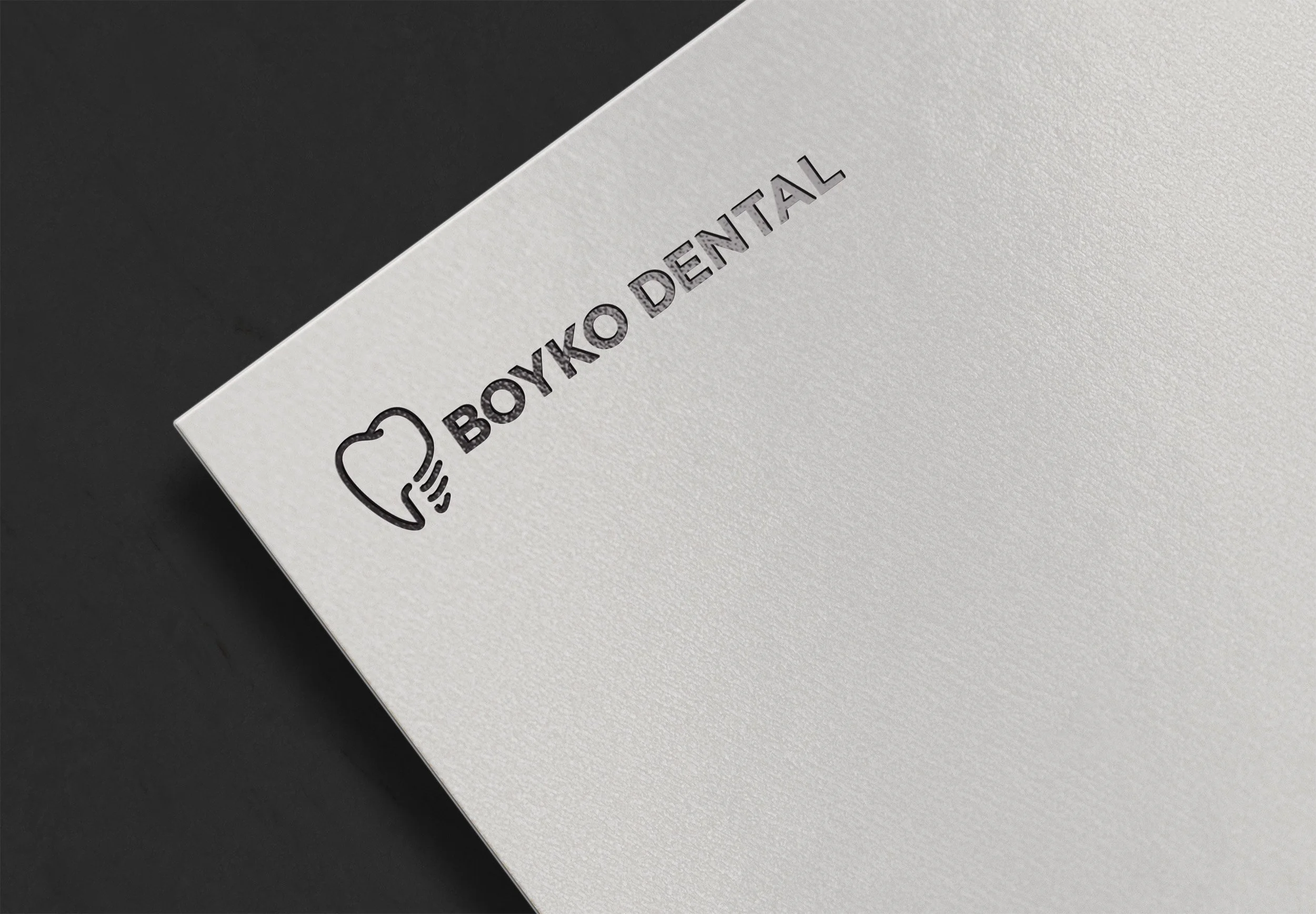 Close-up of a white textured dental business card featuring Boyko Dental logo, a stylized tooth icon and the practice's name in black text. Created by Clarke Creative