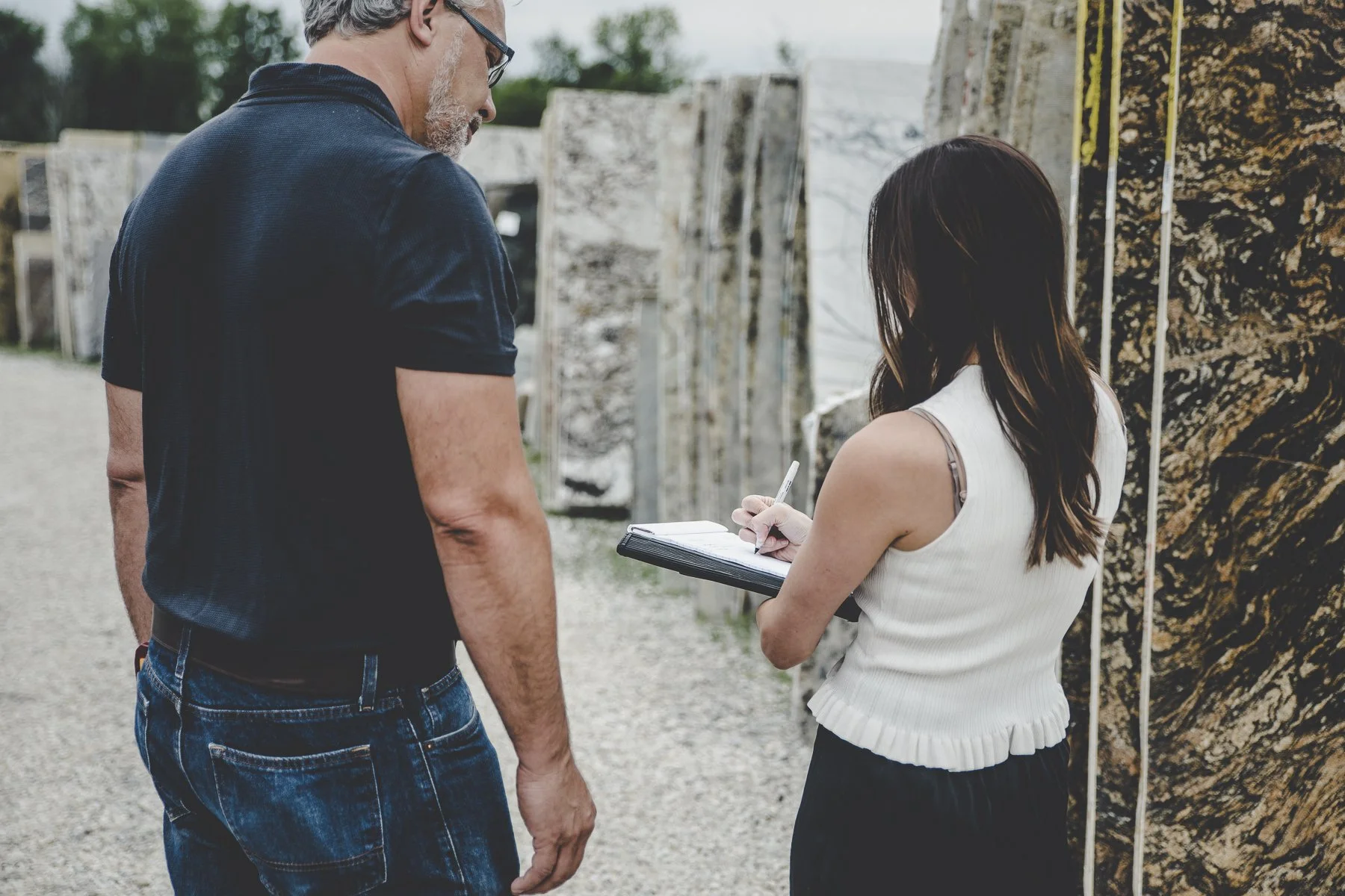Rachelle Clarke and client at a brand strategy meeting, walking through a stone yard with slabs of granite and quartzite. Clarke Creative.