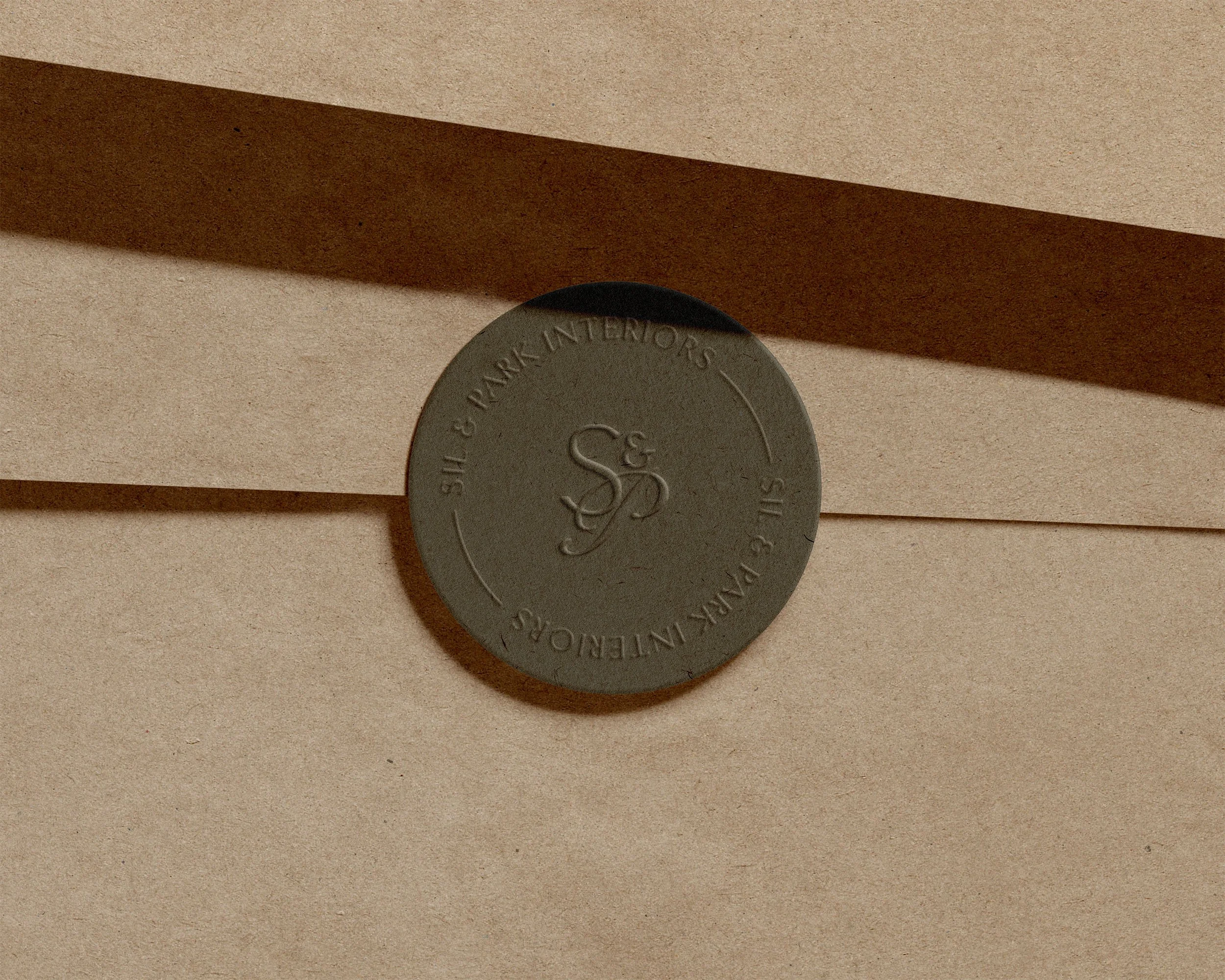 Dark green circular sticker with embossed SIL & PARK Interiors submark logo and text, placed on a cardstock paper envelope. Created by Clarke Creative.