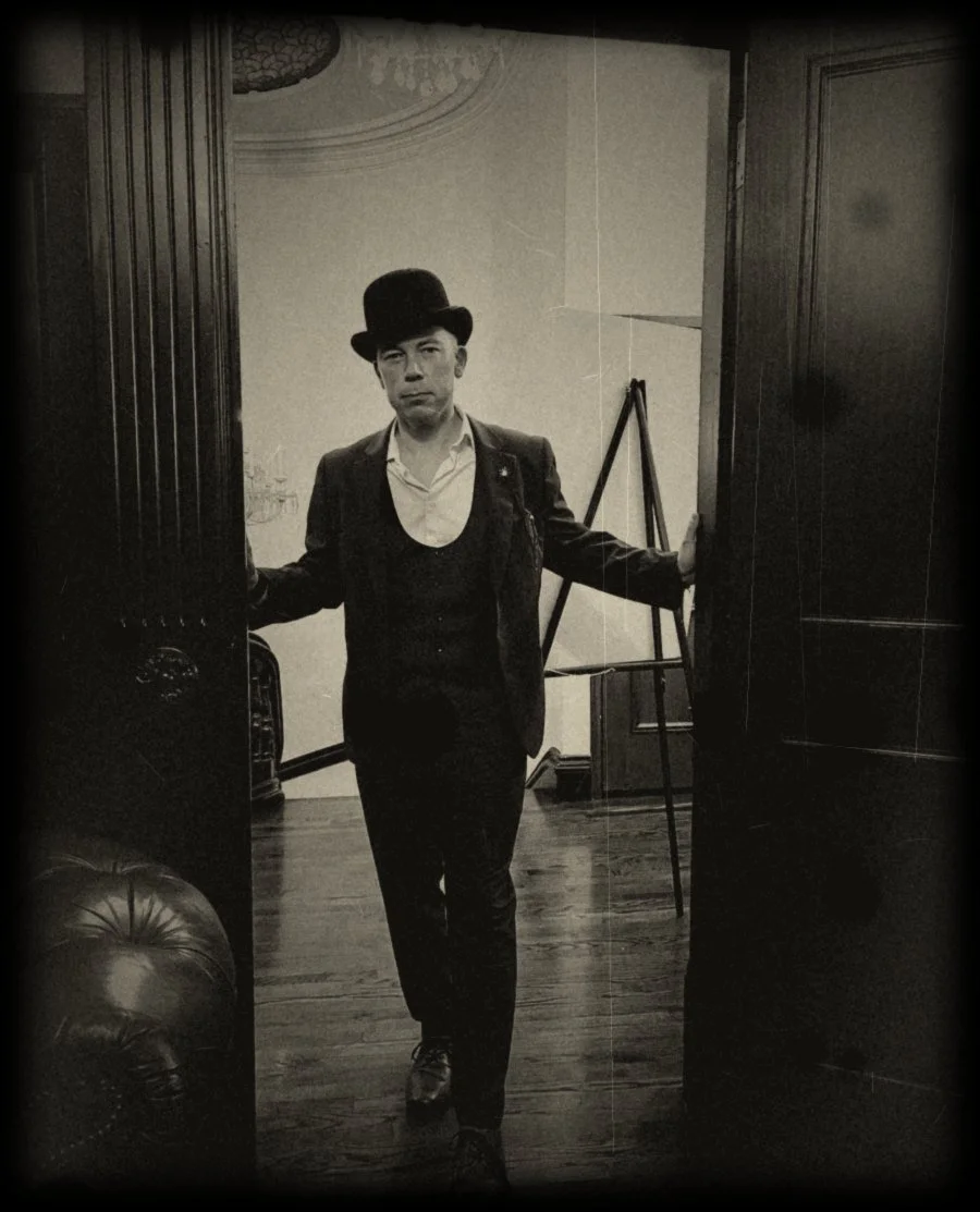 Nolan in a bowler hat standing in a dark wooden doorway