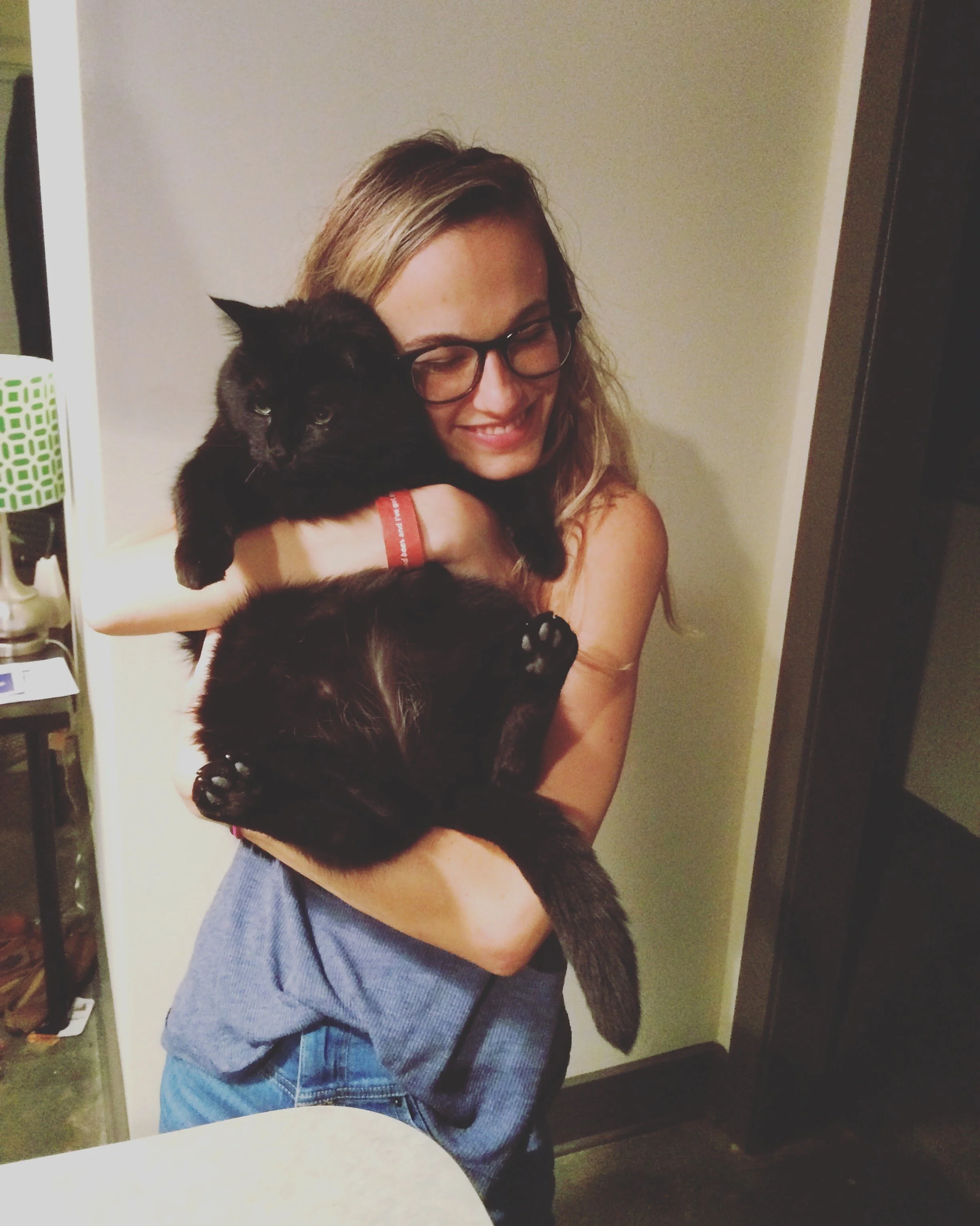 Woman with glasses smiling while holding a black cat inside a home in Raleigh, North Carolina.