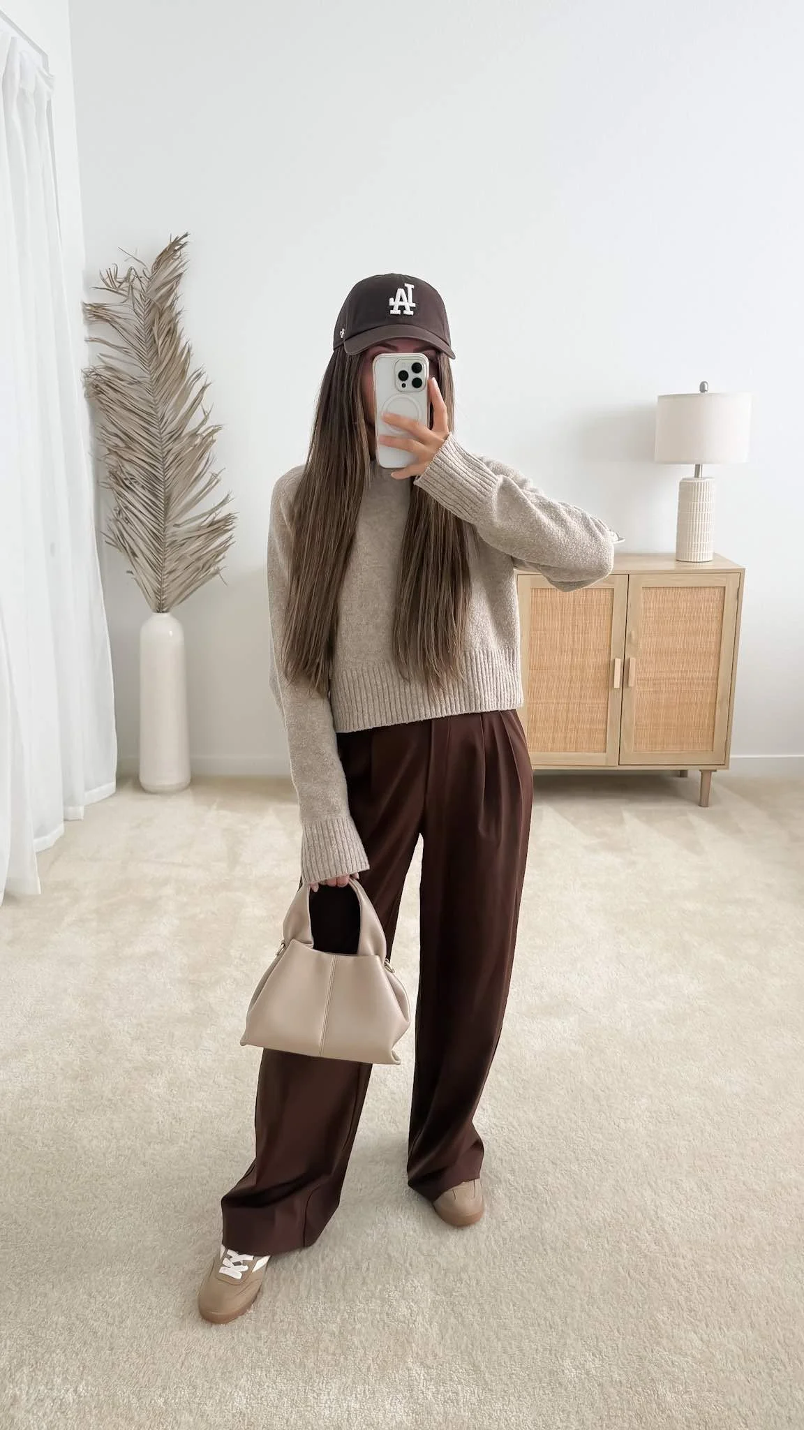 Fall outfit with beige sweater, dark brown wide leg trousers, neutral sneakers, and brown baseball cap