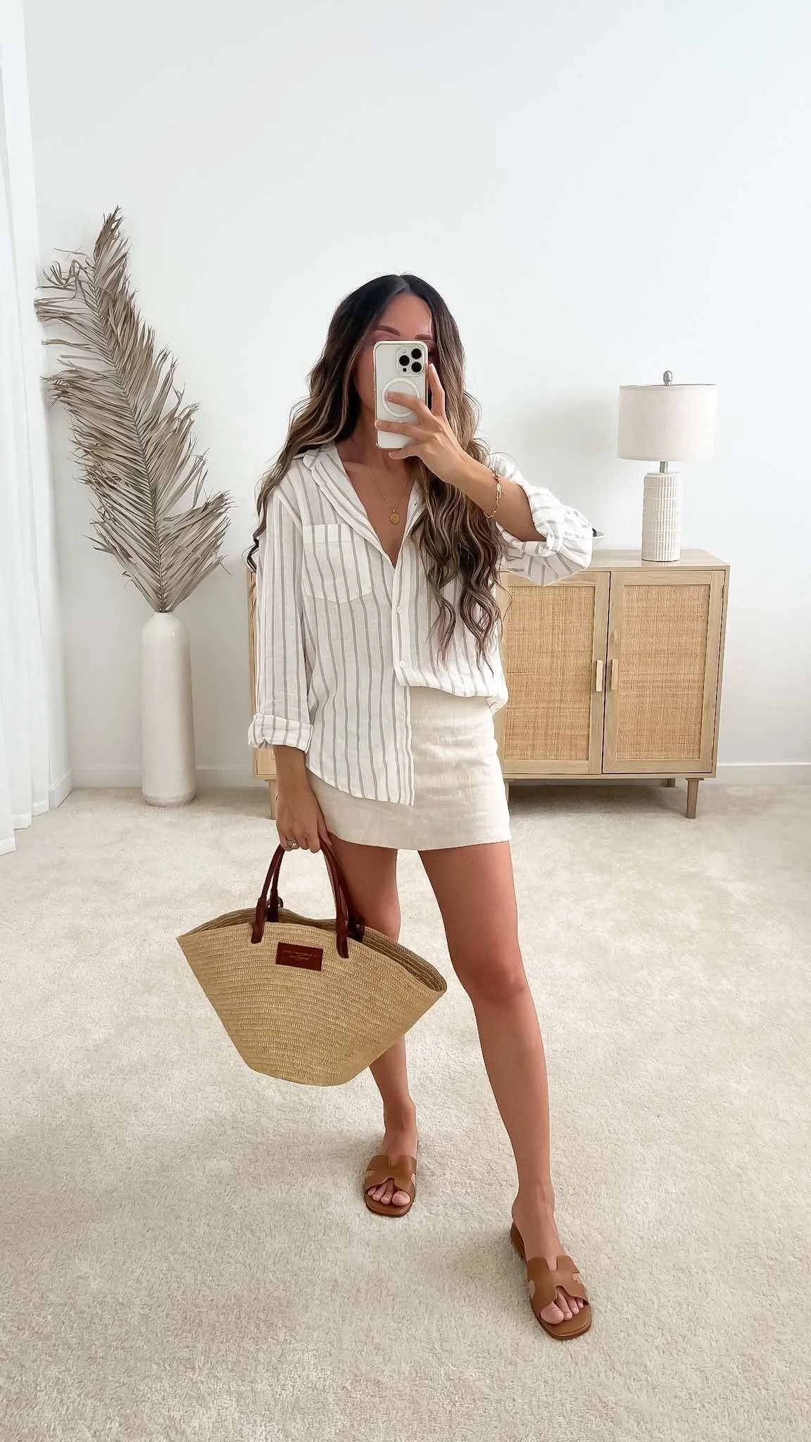 A neutral summer capsule outfit featuring a striped linen button-down shirt, tan mini skirt, and the Sézane Justine bag