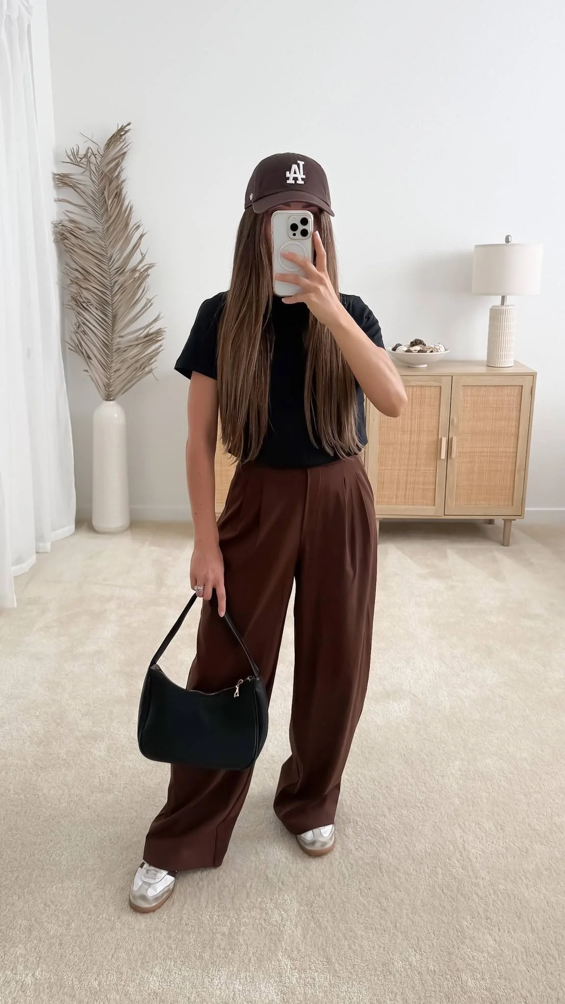 Warm weather fall outfit with black t-shirt tucked into brown trousers, adidas samba sneakers, faux leather purse and brown baseball hat