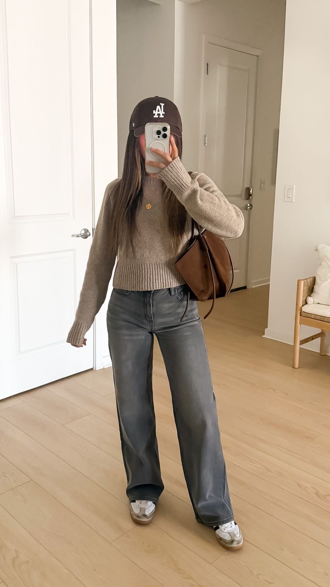 Casual fall outfit with beige sweater, gray wide-leg jeans, neutral sneakers and brown suede bag