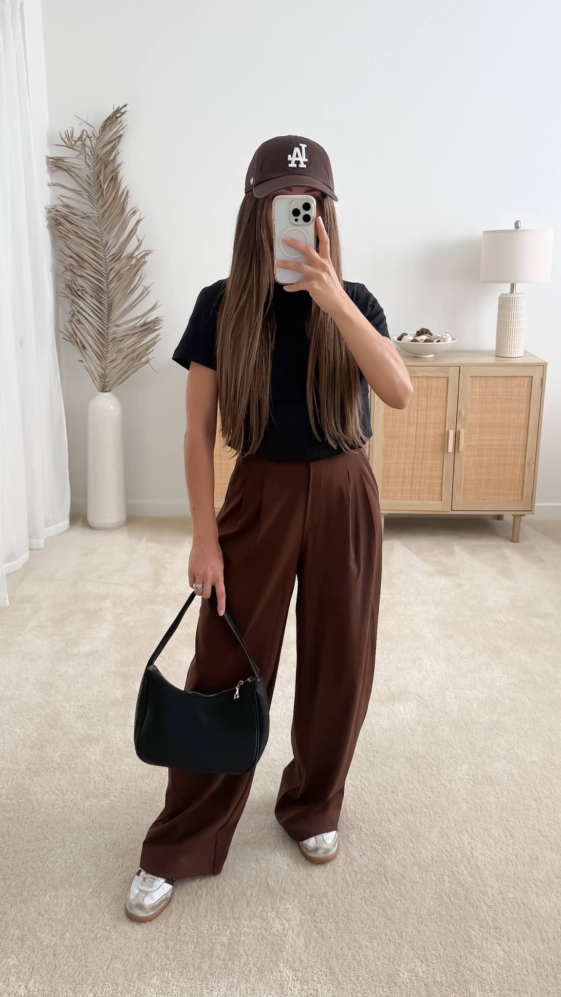Brown pants outfit styled with brown trousers, a black T-shirt, white sneakers, black shoulder bag and brown baseball cap