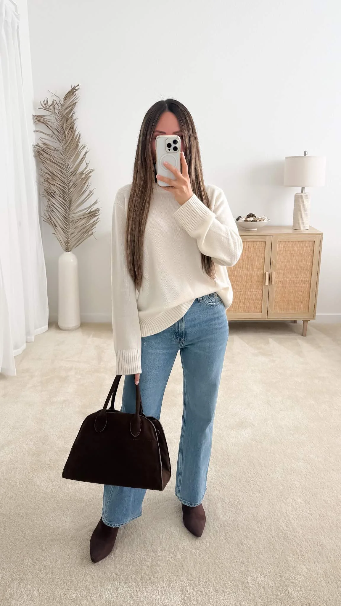 Cream sweater styled with light wash wide leg jeans, brown ankle boots, and a brown suede handbag.