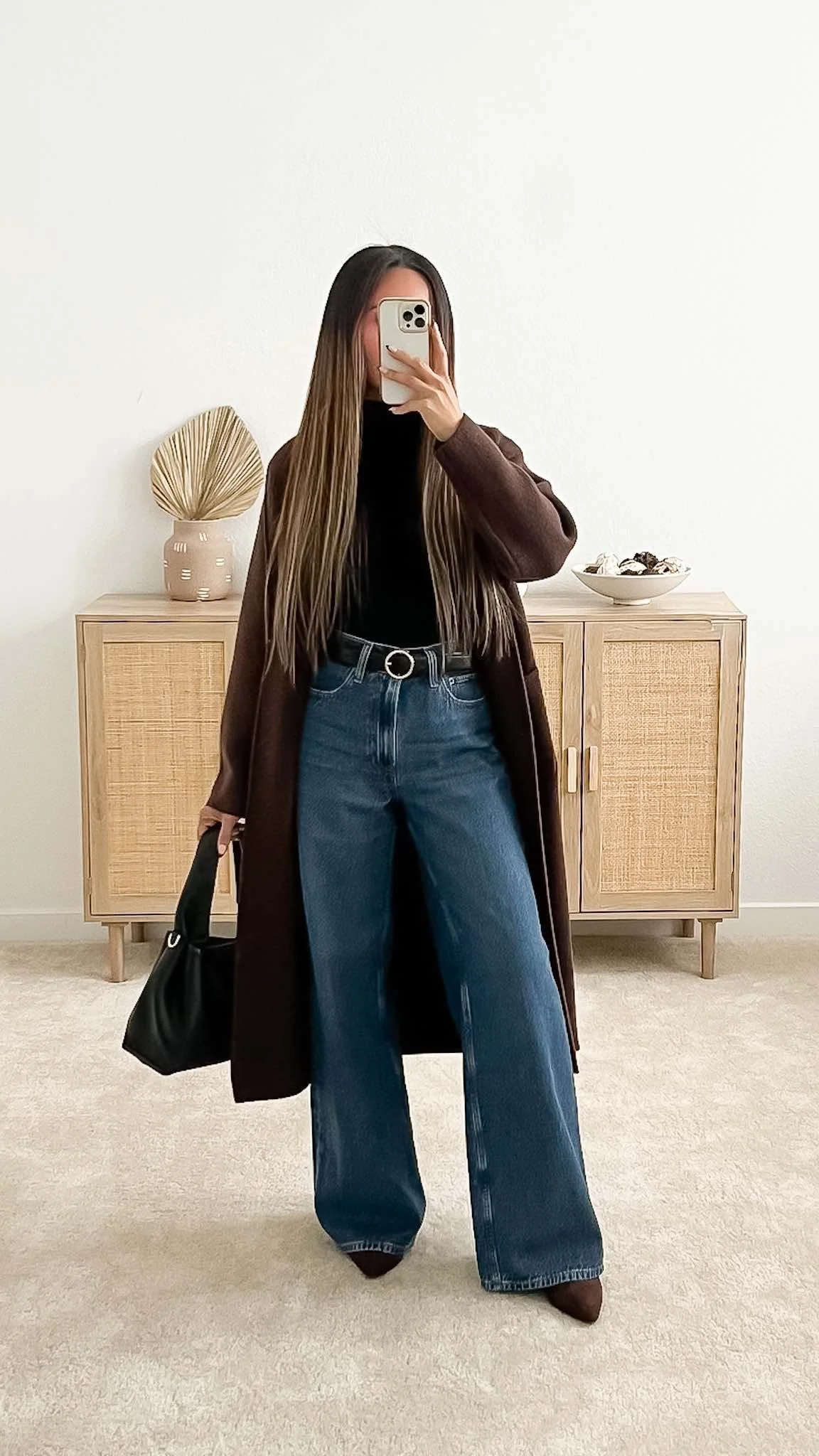 Fall date outfit with a long brown cardigan, black mockneck bodysuit, wide-leg jeans, pointed brown boots, and a black handbag