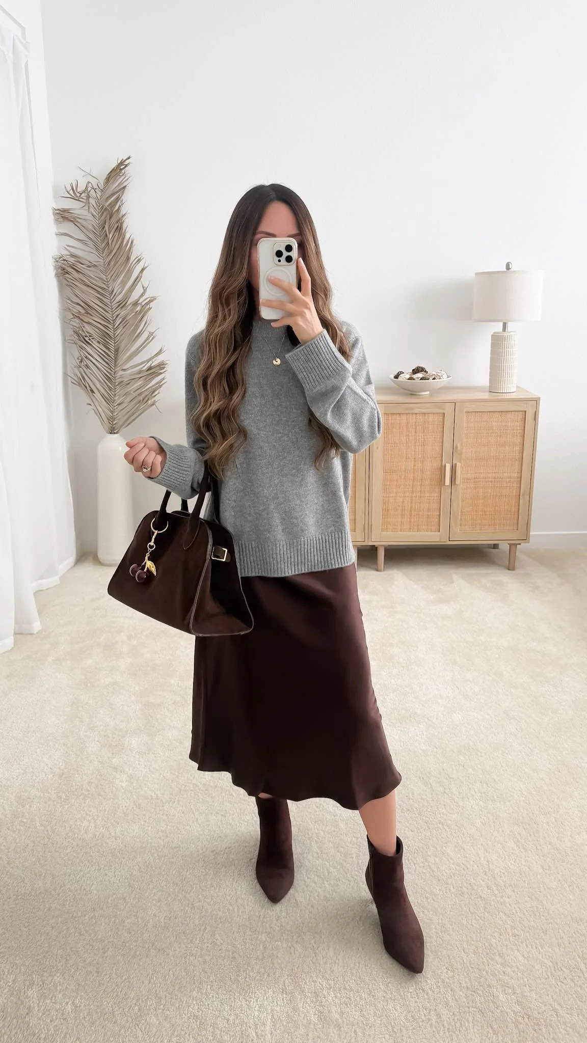 Sweater with satin skirt outfit featuring Quince Mongolian Cashmere Oversized Crewneck Sweater styled with a brown satin midi skirt, brown ankle boots, and a matching handbag