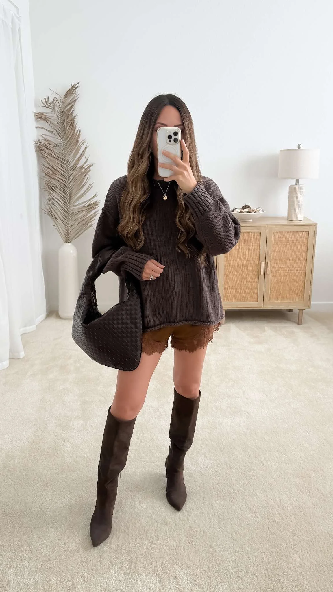 Fall going-out outfit with an oversized brown sweater, lace-trim shorts, pointed knee-high boots, and a woven handbag