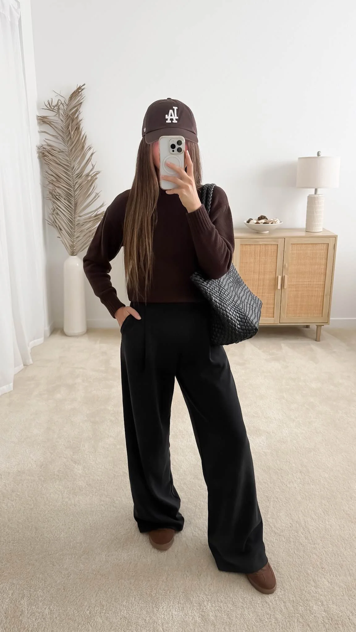 Fall outfit with dark brown sweater, black tailored wide-leg pants, brown sneakers, baseball cap and black woven tote