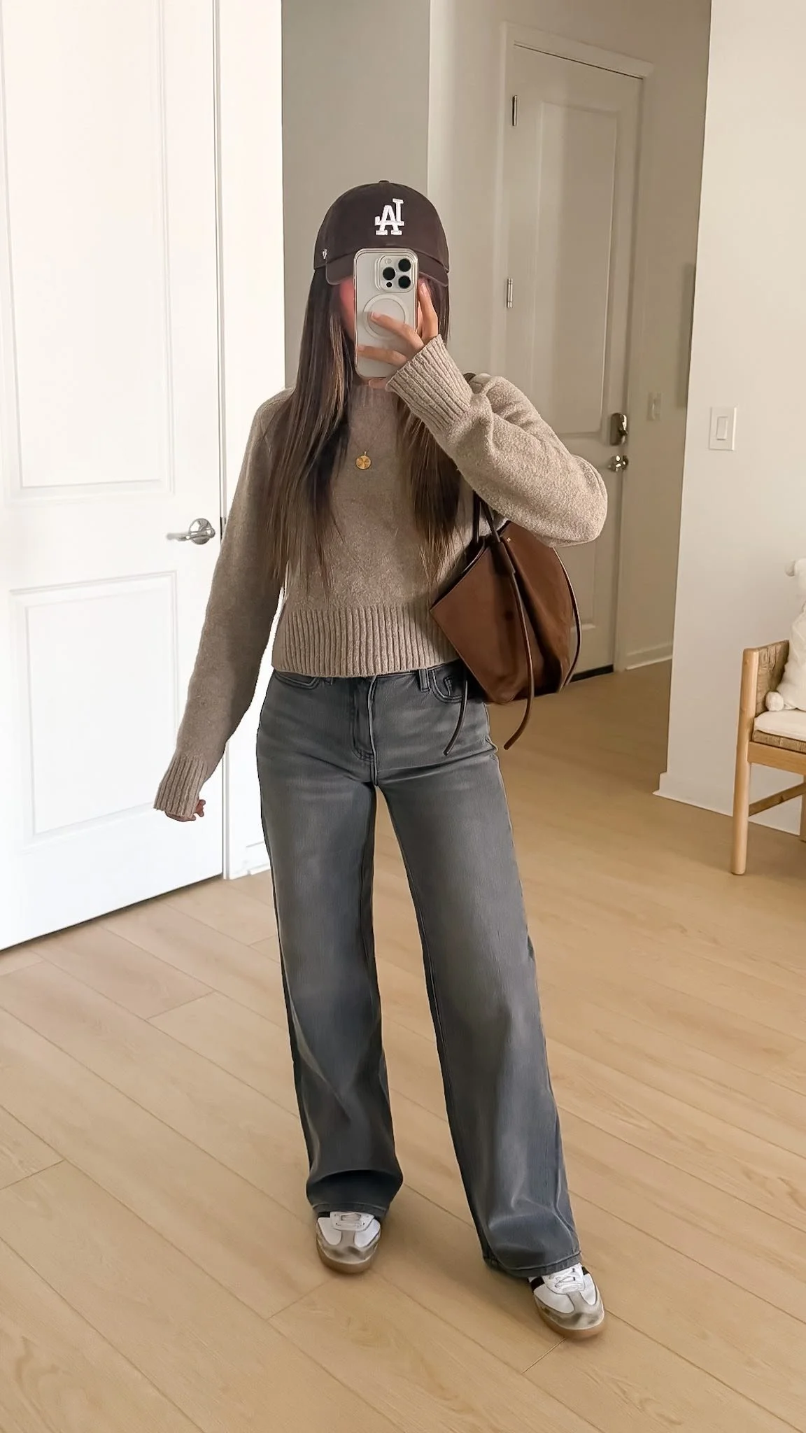 Gray relaxed straight leg jeans with a neutral sweater, white sneakers, and a brown shoulder bag for a casual fall outfit.