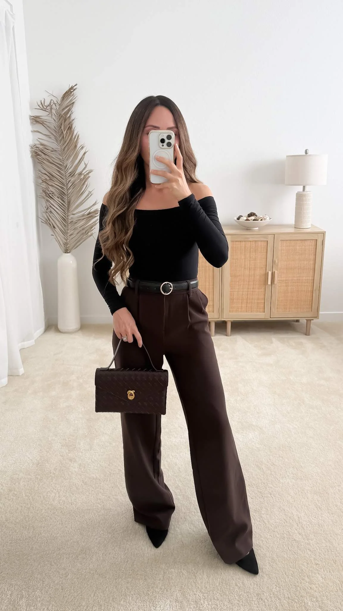 Fall date night outfit with a black off-the-shoulder top styled with dark brown wide-leg trousers, black pointed heels, and a brown woven clutch