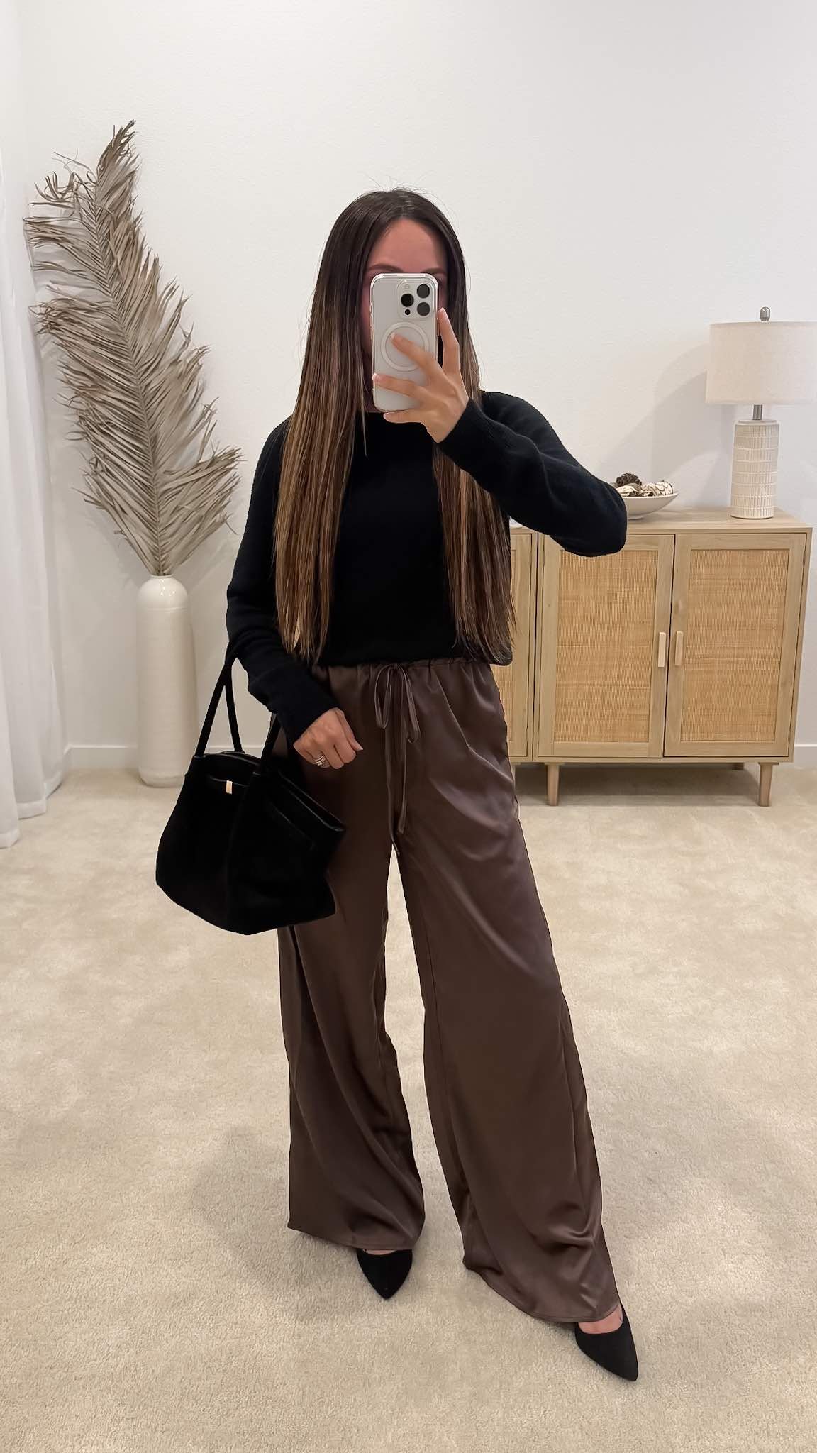 Brown pants outfit styled with brown satin wide-leg pants, a black sweater, black pointed-toe heels and black tote bag