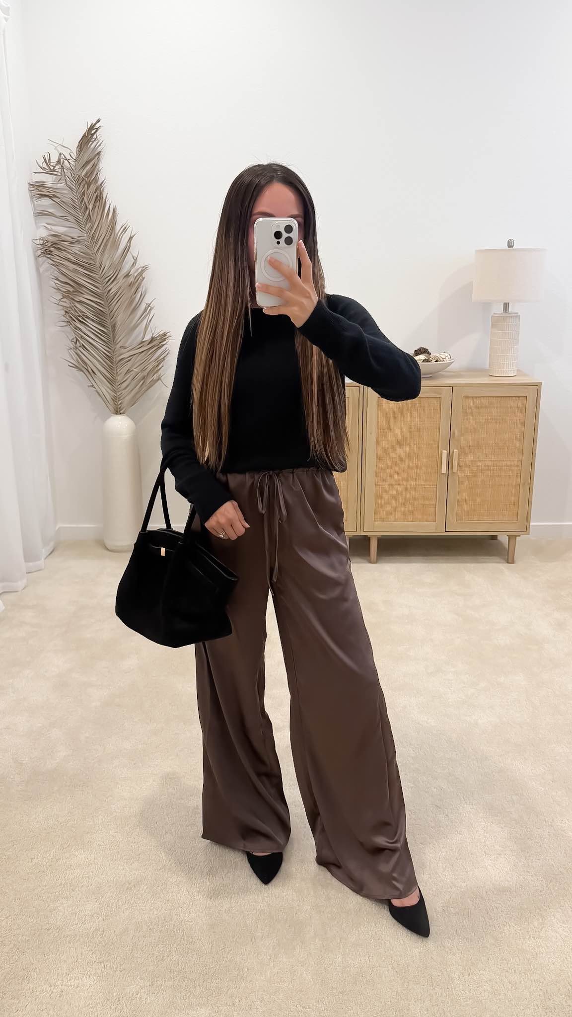 Fall date night outfit idea with a black sweater, chocolate brown satin wide-leg pants, pointed heels, and a black tote