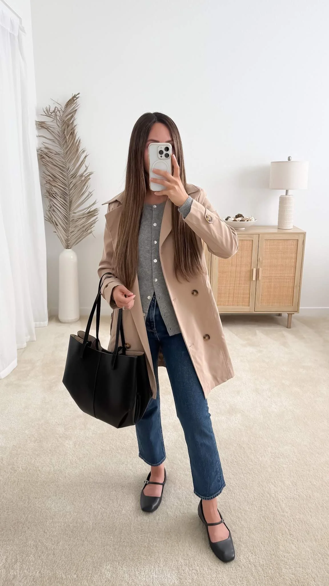 Beige trench coat outfit with a gray cardigan, straight-leg jeans, and black ballet flats.