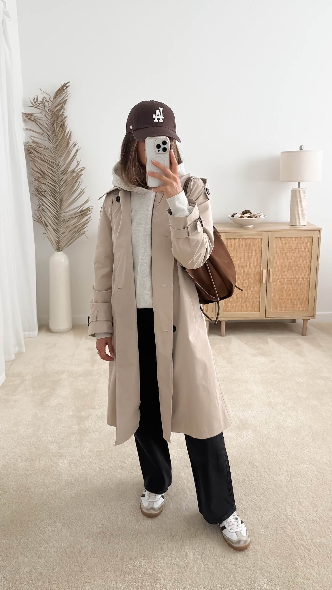 Casual fall outfit with beige trench coat, gray hoodie, black jeans and neutral sneakers