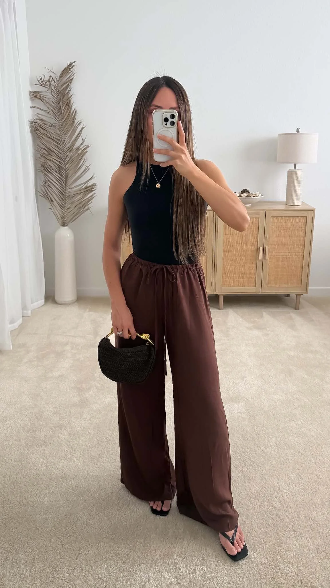 Brown linen pants outfit styled with a black tank top, black sandals, and woven handbag for summer