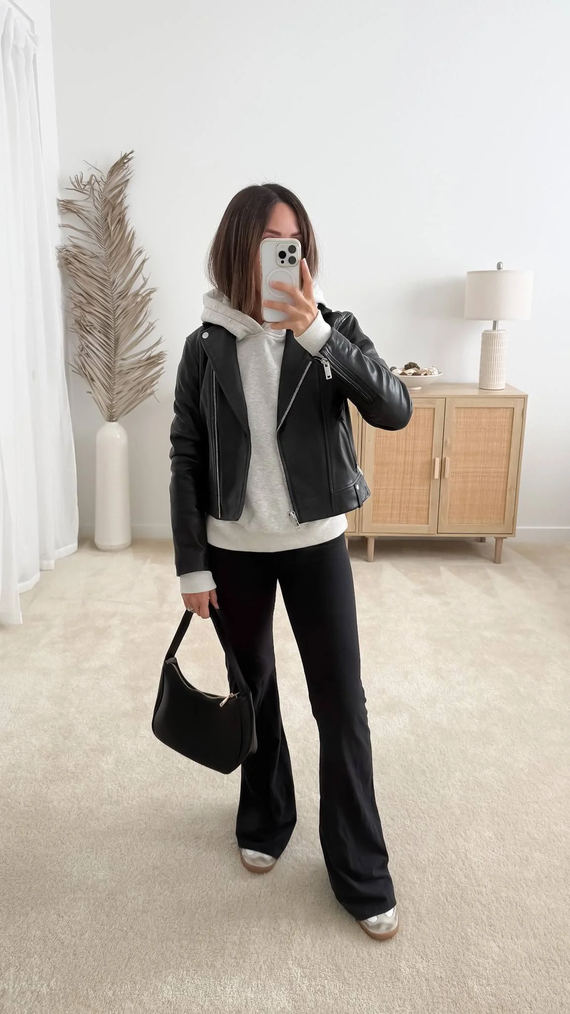 Leather jacket outfit with black leather jacket layered over grey hoodie, flare leggings, adidas samba sneakers, and black faux leather purse